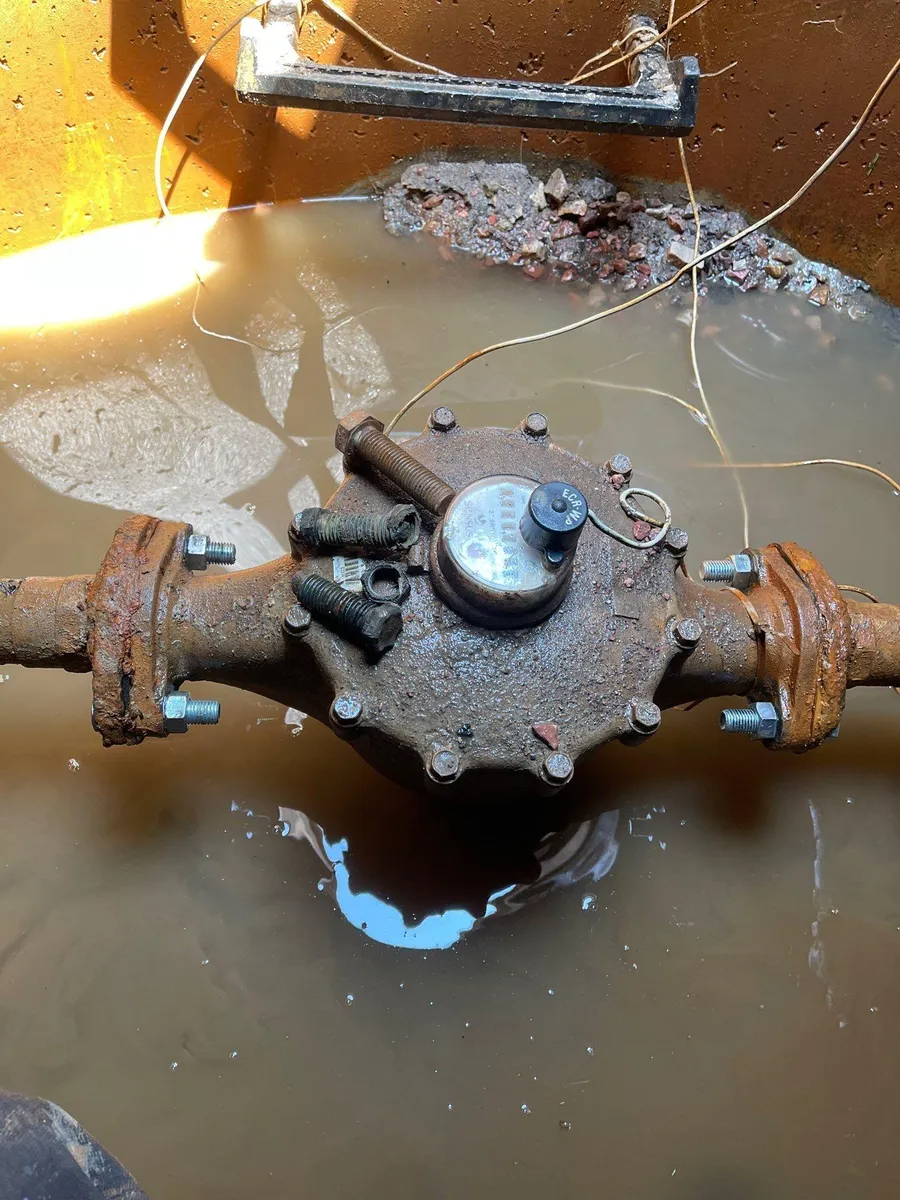 Rusty old valve on a corroded pipe in muddy water, with a blue handle and debris around it