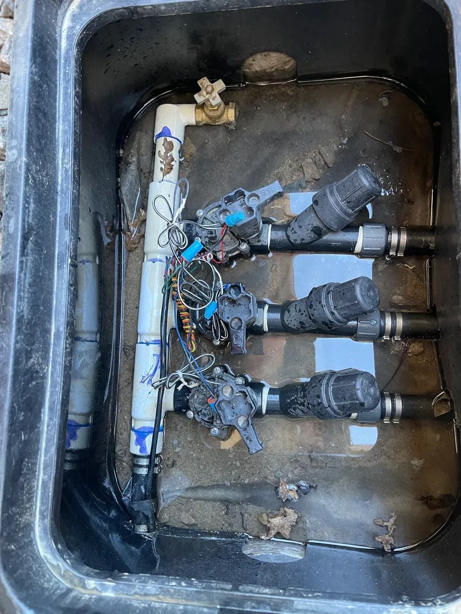 Open utility box with tangled wiring, valves, and muddy water inside