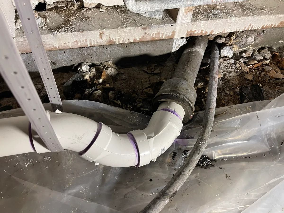 Exposed white PVC drain pipe under a sink with a dark, broken opening in the wall behind it