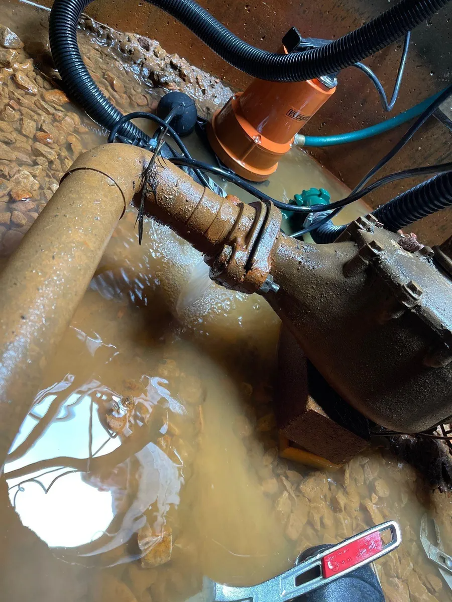 Rusty pipe under muddy water with a valve and hoses in a flooded utility space