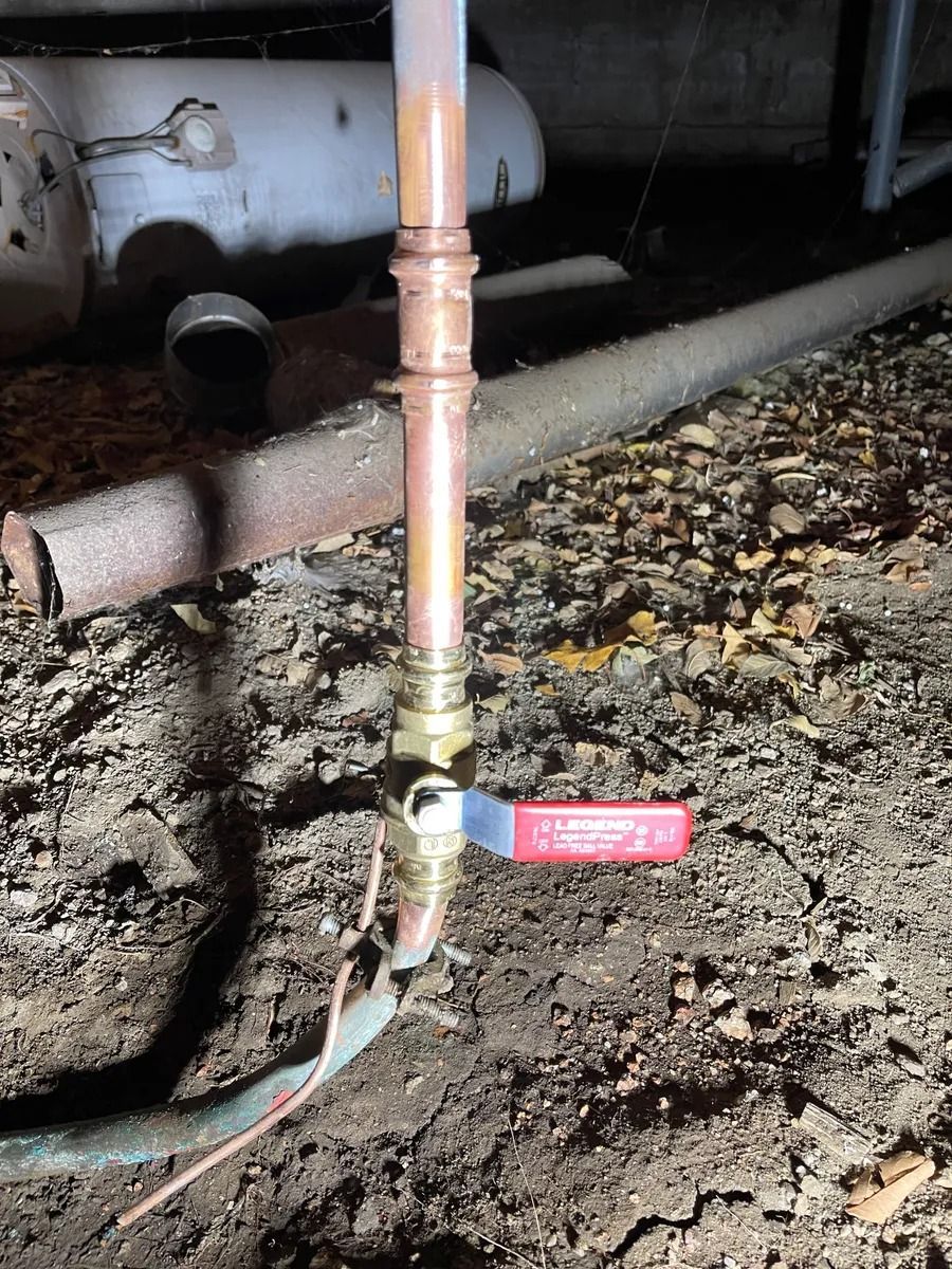 Red-handled valve on a copper pipe in a muddy industrial area, with hoses and pipes in the background