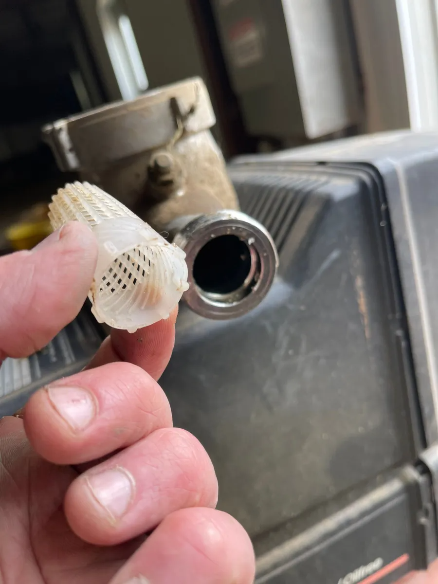 Hand holding a small white plastic connector near a metal pipe opening in a kitchen sink area