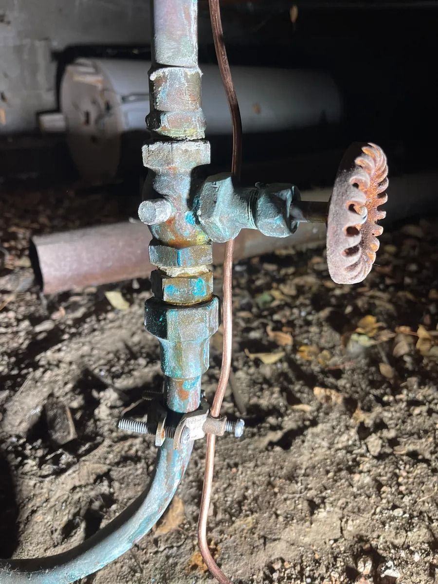 Rusty outdoor water valve with a blue hose attached and a metal handwheel on dirt ground