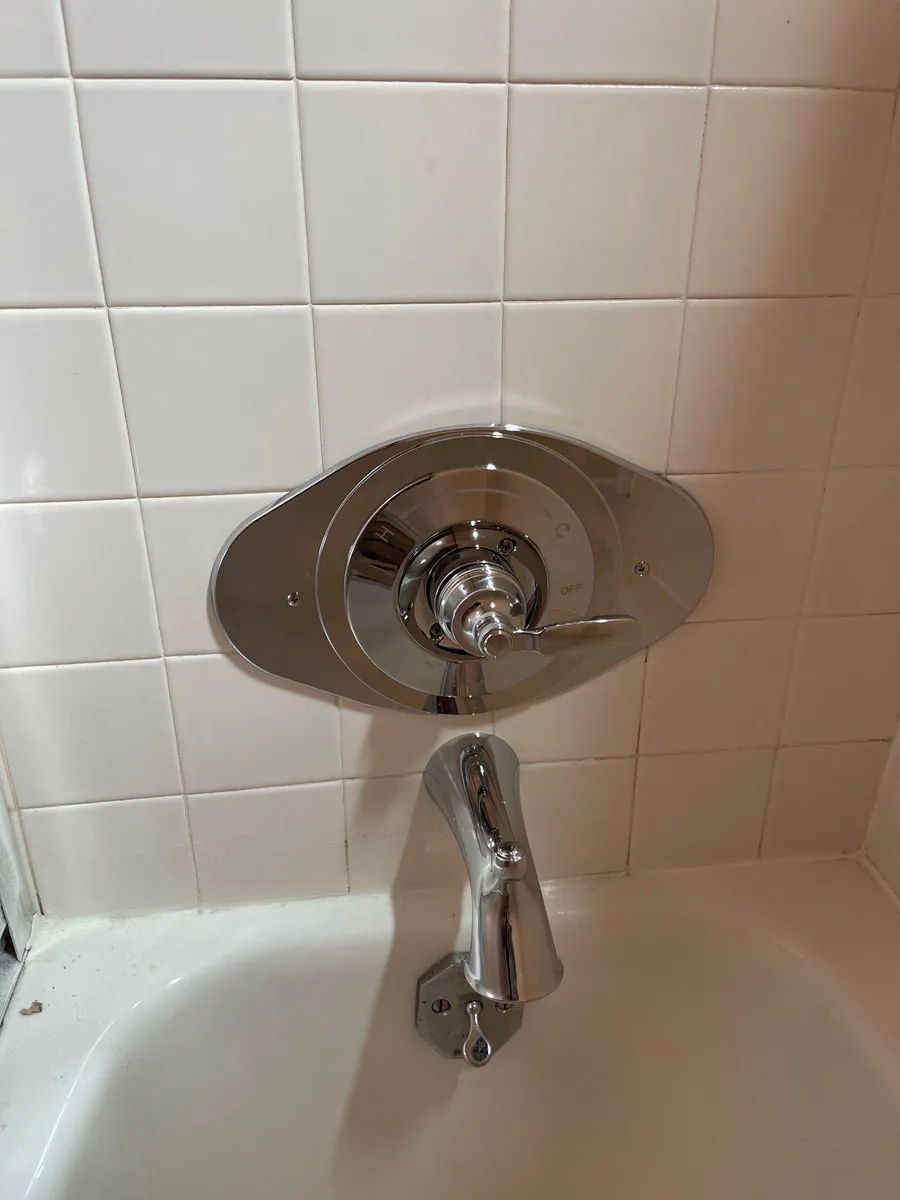 Close-up of a chrome bathtub faucet and knob on white tiled bathroom wall