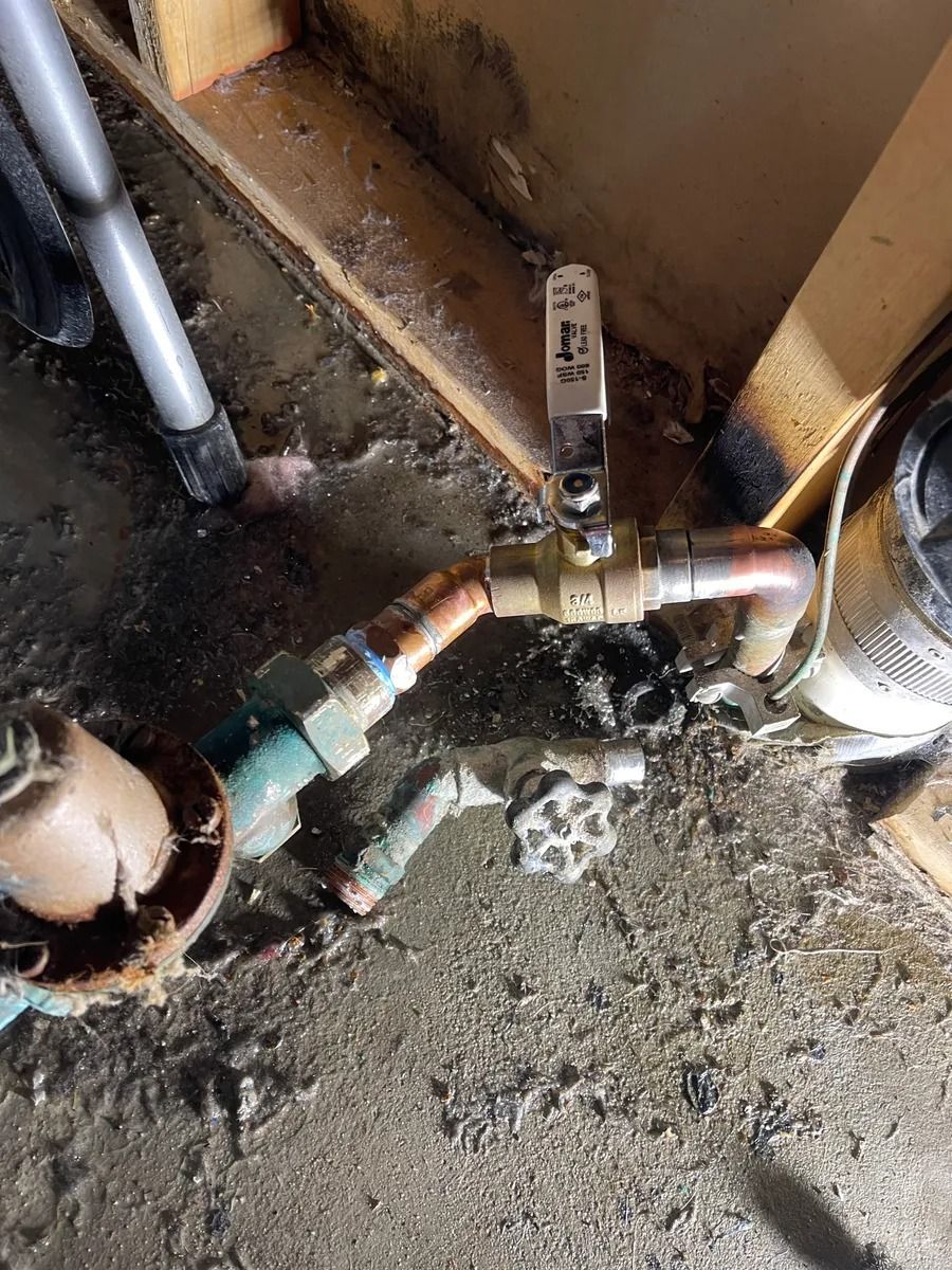 Leaking brass pipe valve and fittings over a wet concrete floor in a utility area