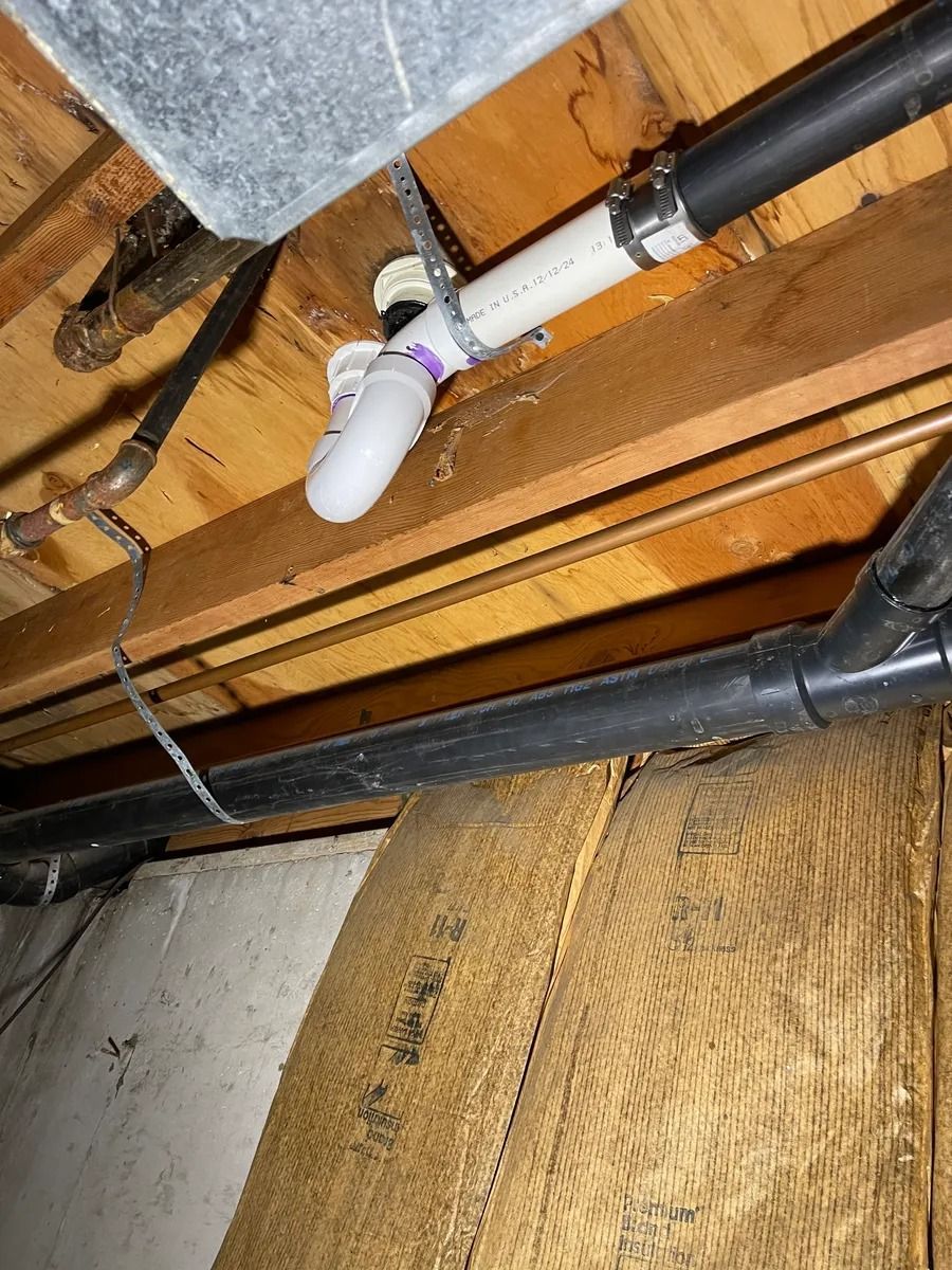 Basement ceiling with exposed pipes and a white PVC drain fitting near insulation.