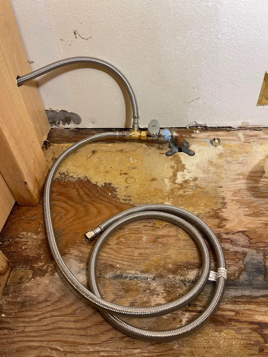 Coiled metal pipe on a dusty floor beside a wall and wooden baseboard, with a faucet valve attached