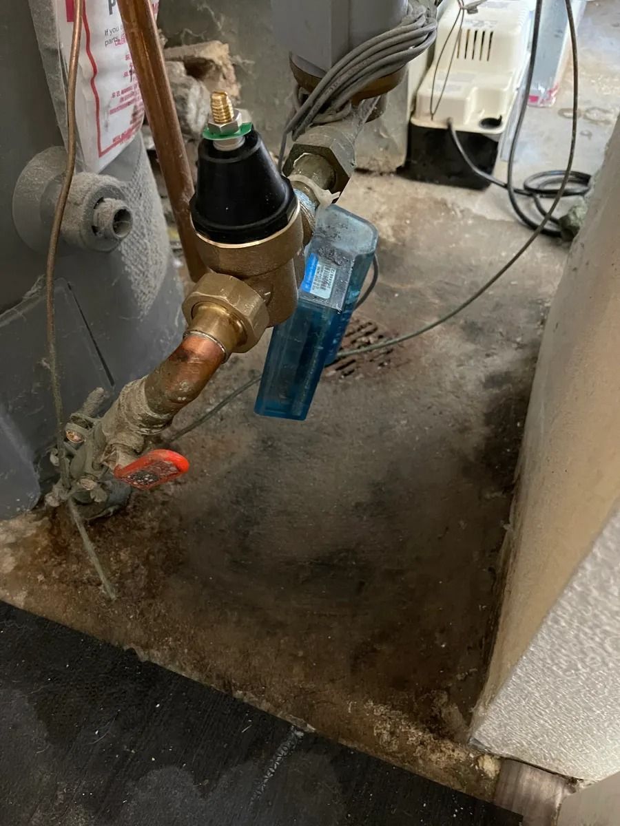 Close-up of a brass water valve and blue meter in a utility area with dusty concrete floor
