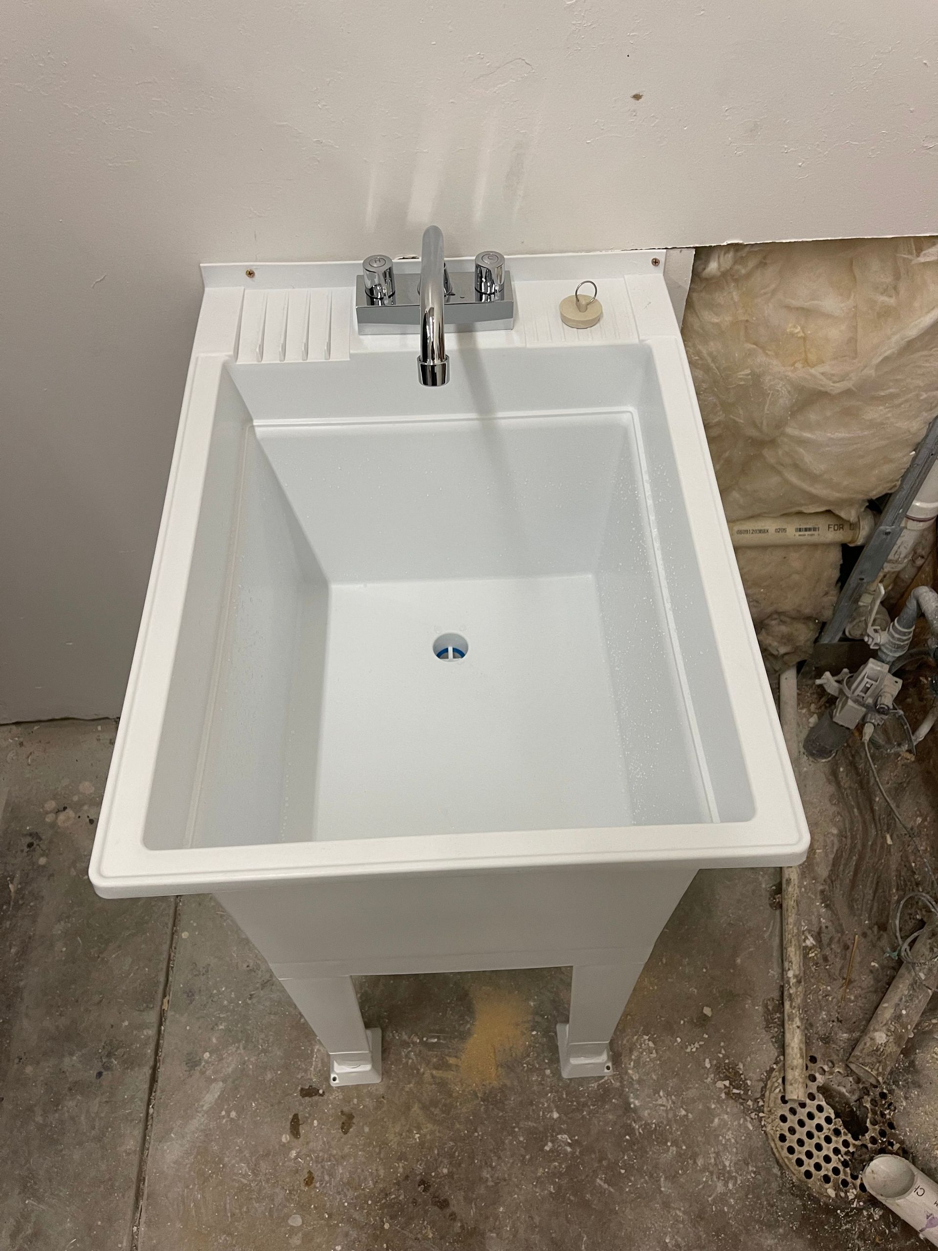 White utility sink with faucet in a partially renovated room, next to exposed insulation and unfinished walls