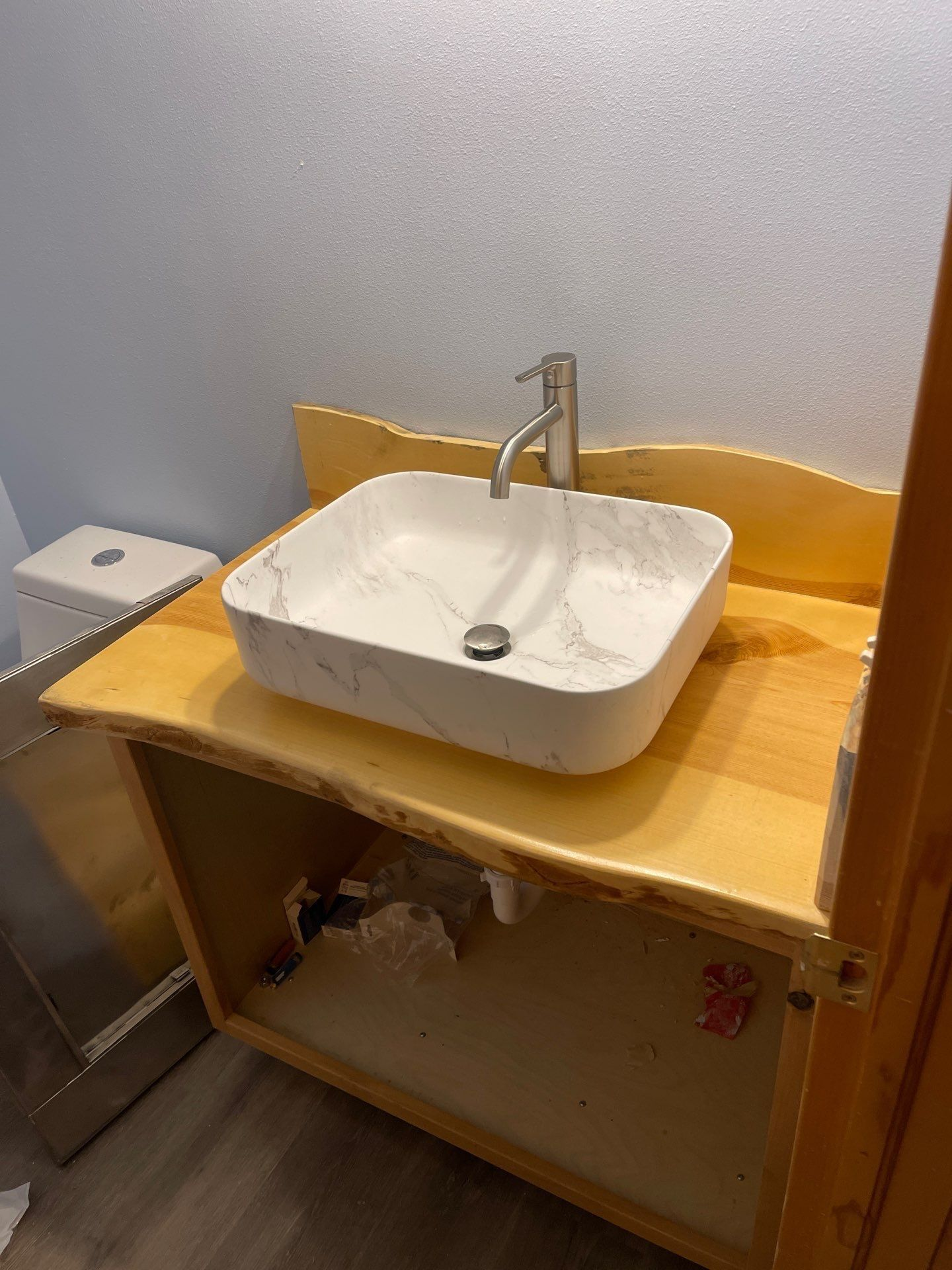 White sink on wooden cabinet with open storage against a gray wall in a bathroom.
