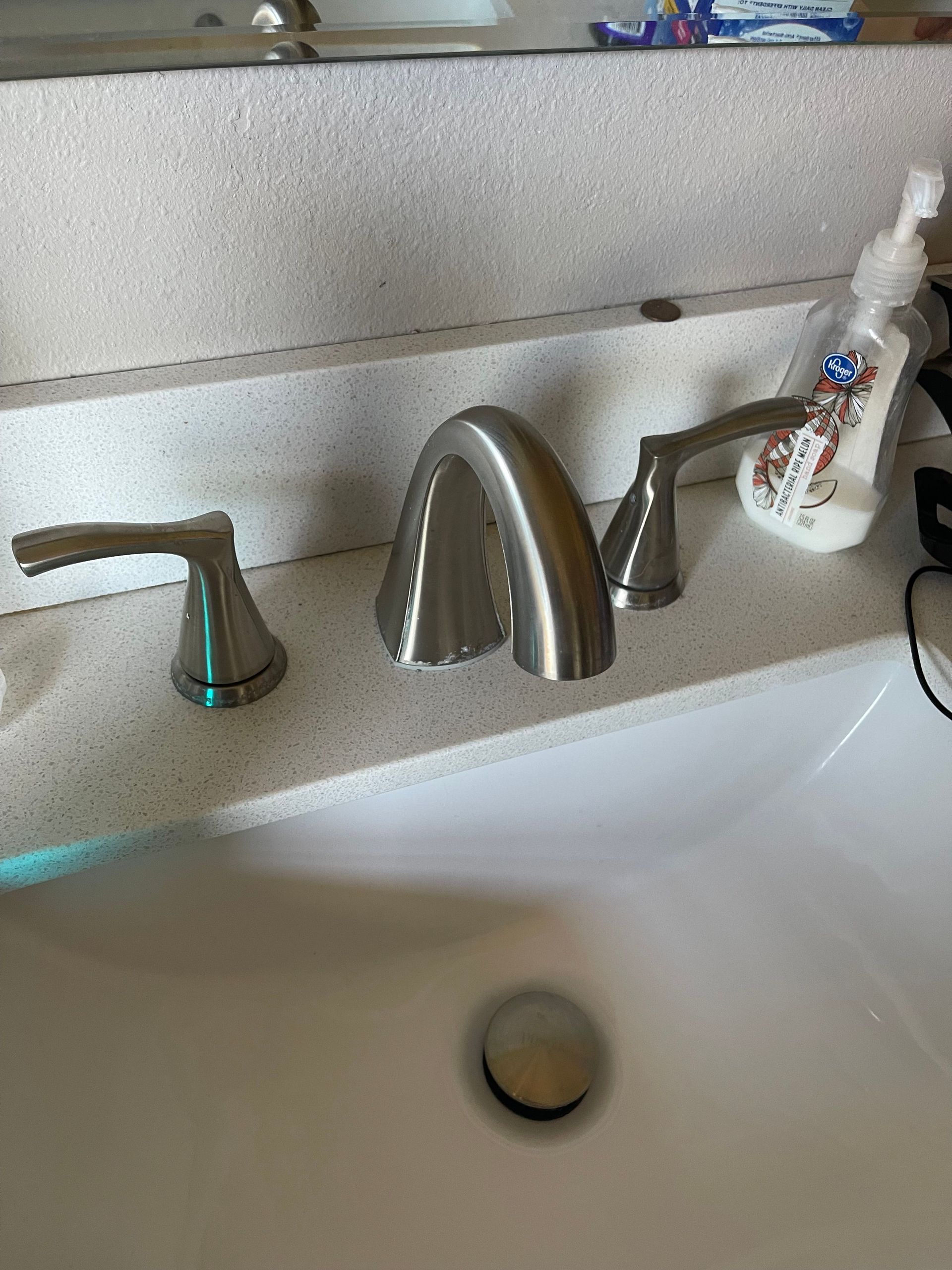 Bathroom sink with chrome faucet and soap dispenser on a white countertop.