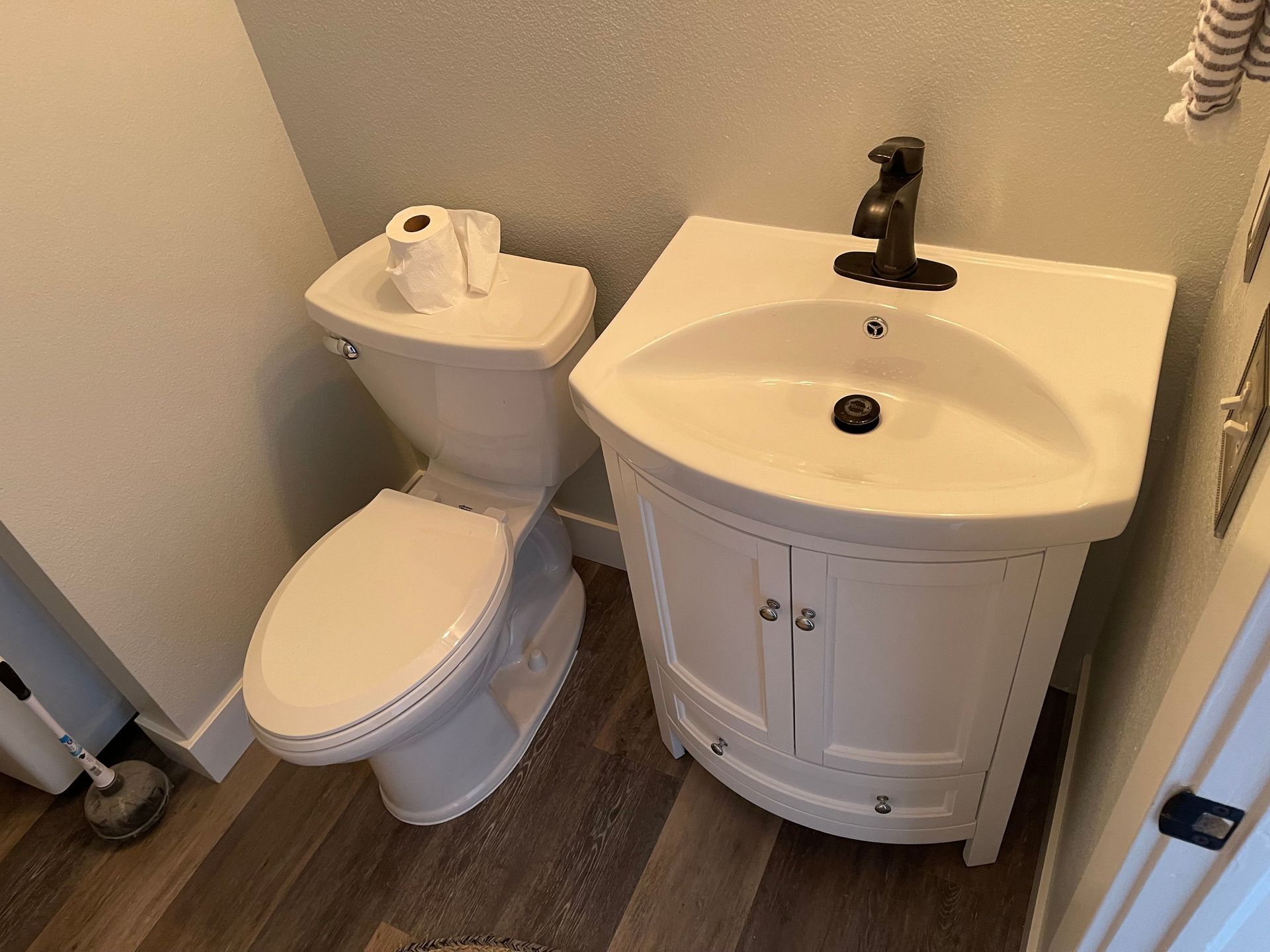 Small bathroom with a toilet, white sink cabinet, and wood-look flooring.