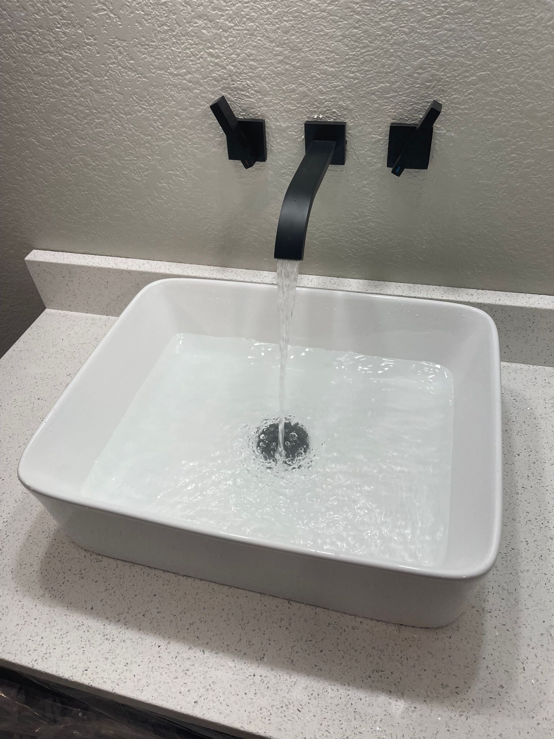 White bathroom sink under a black faucet with water running into it.