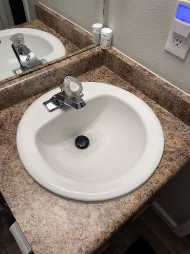 Bathroom sink with speckled countertop, mirror, and soap dispenser on the wall.