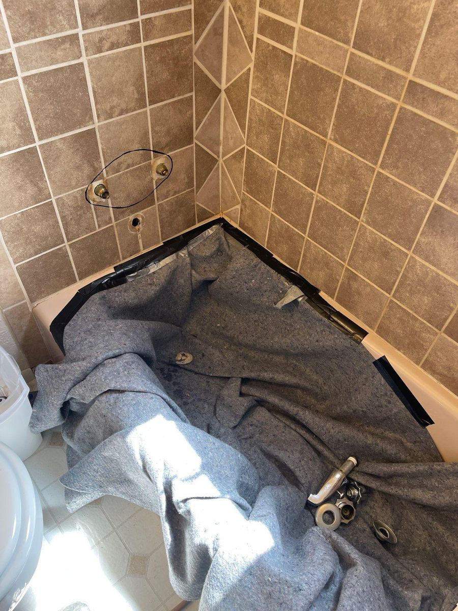 Bathroom shower corner with a blue towel spread on the floor and a detached shower fixture nearby