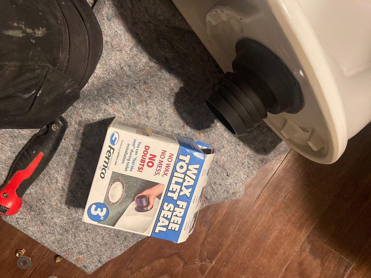 Black-and-white appliance with a wheel, next to a Red Bull can, red tool, and a small booklet on a wooden floor