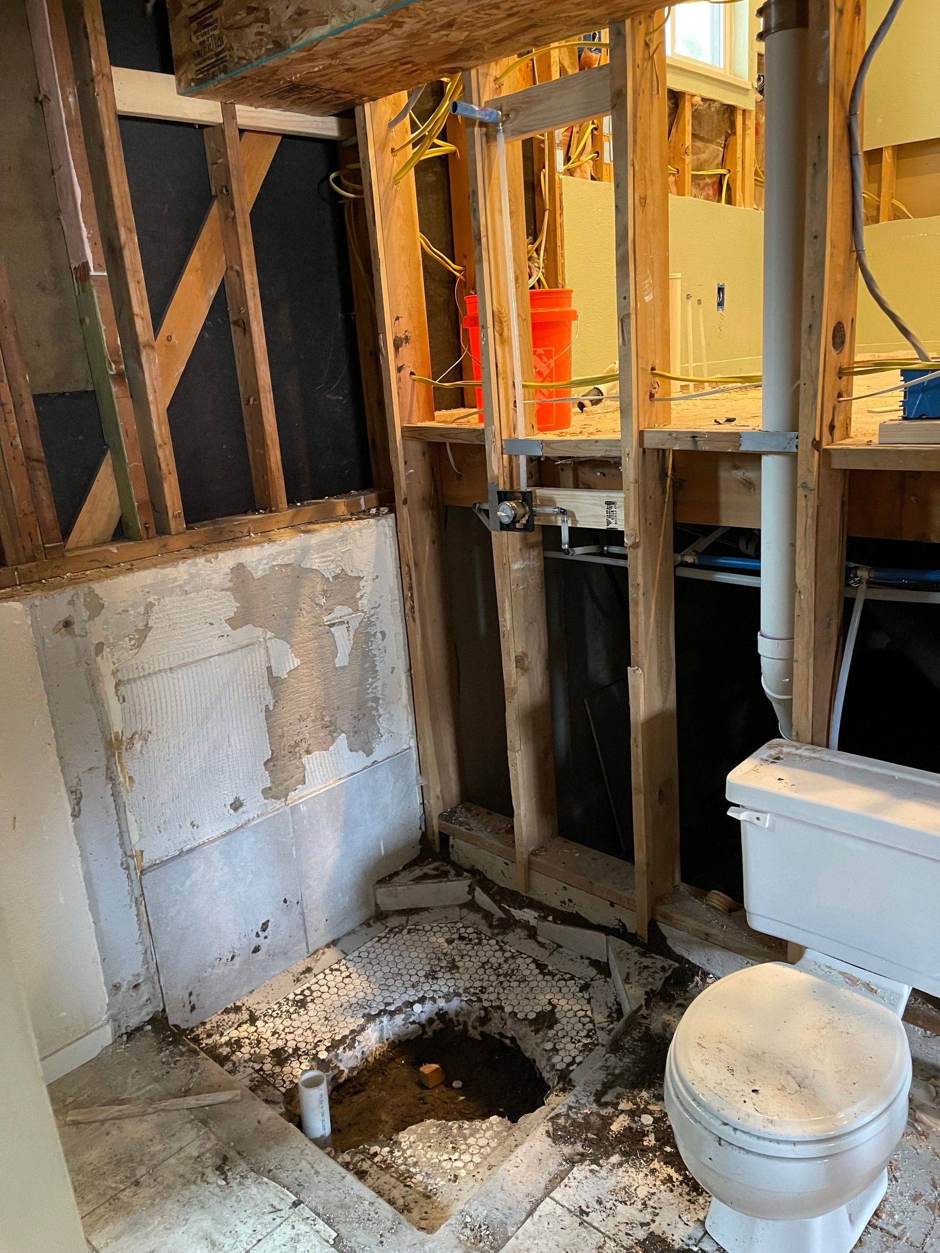 Damaged bathroom with exposed studs, broken floor opening, toilet, and debris from demolition