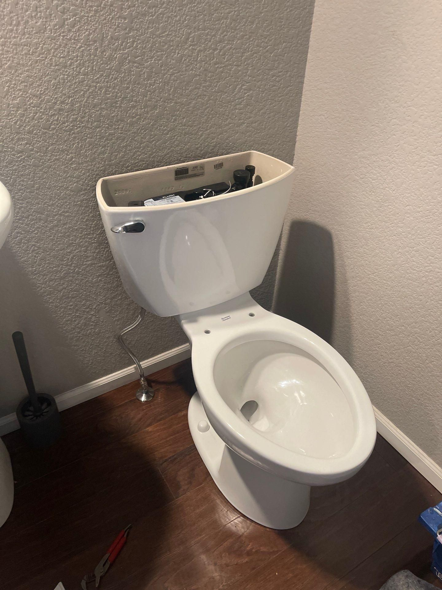 Damaged white toilet in a small bathroom, with the tank lid removed and tools on the floor