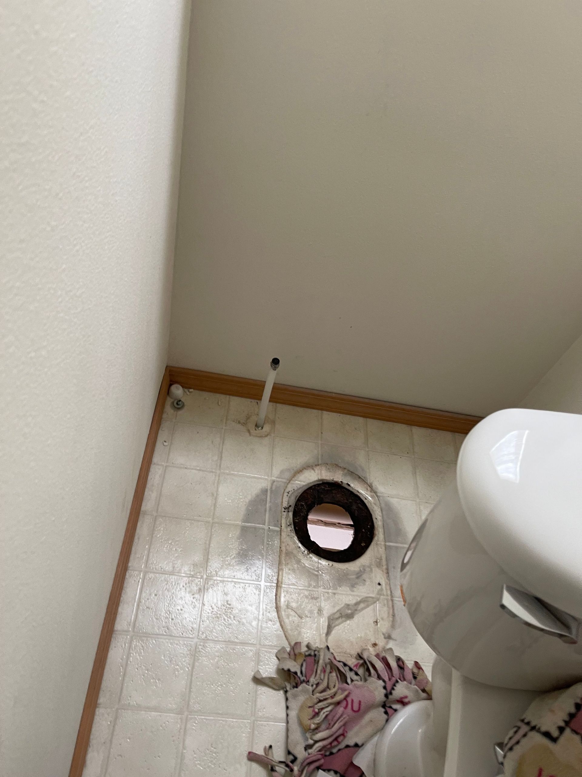 Bathroom floor with a toilet drain cutout, wet tiles, and a small pile of debris or cloth near the wall.