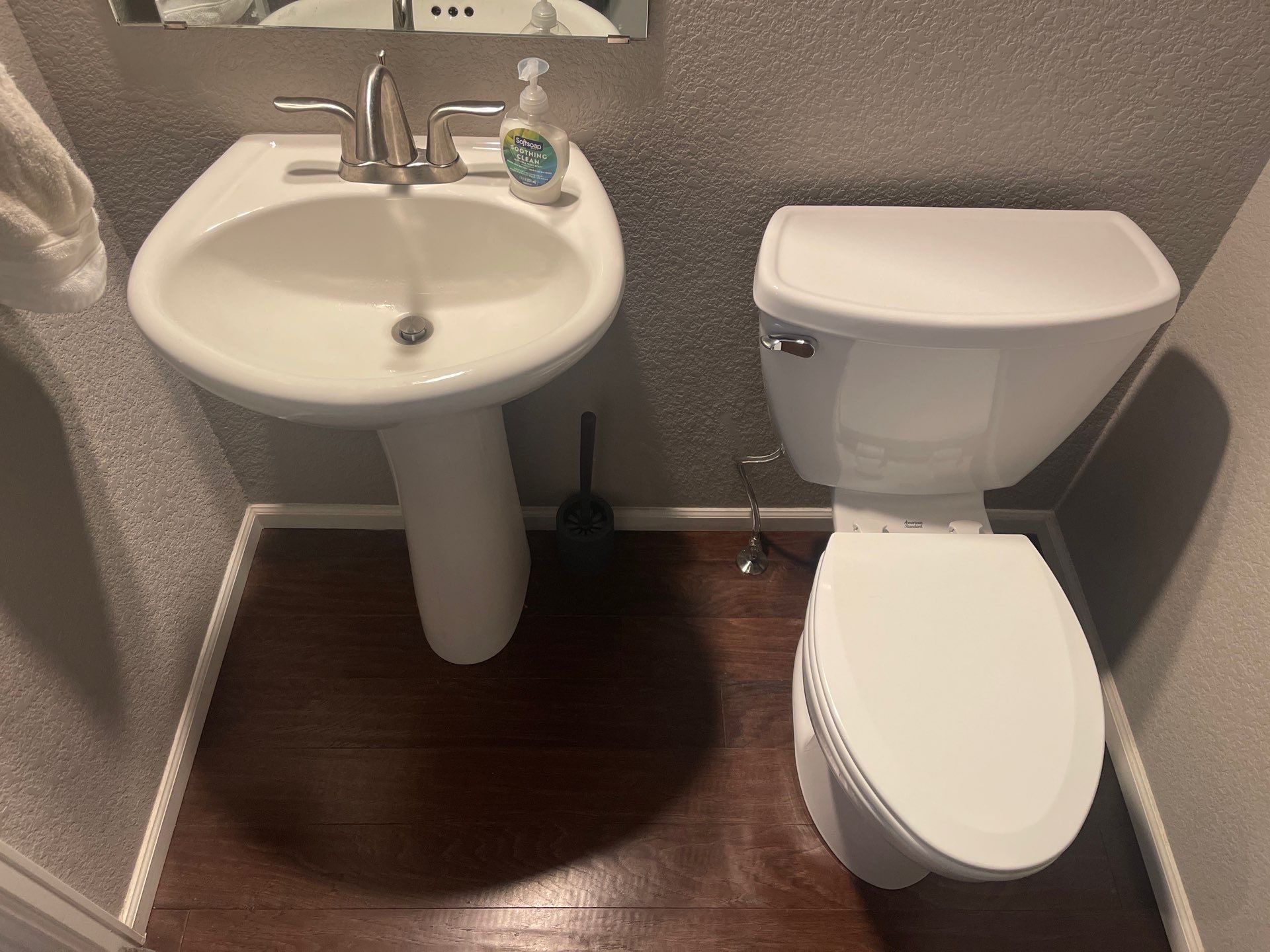 Small bathroom with a white pedestal sink and toilet on a dark wood floor.