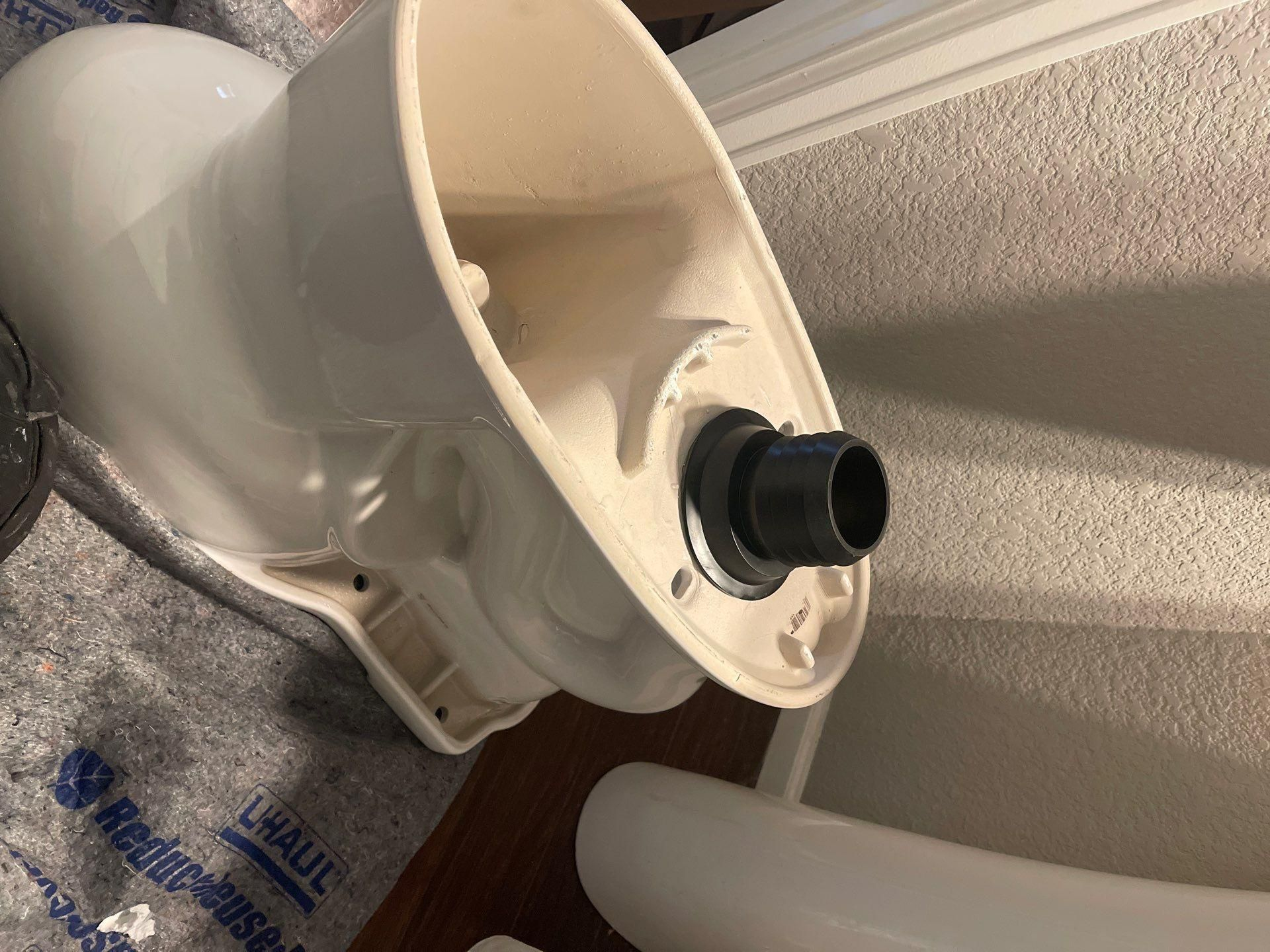 White plastic toilet tank with a black fill valve, shown on a wood floor near a wall.