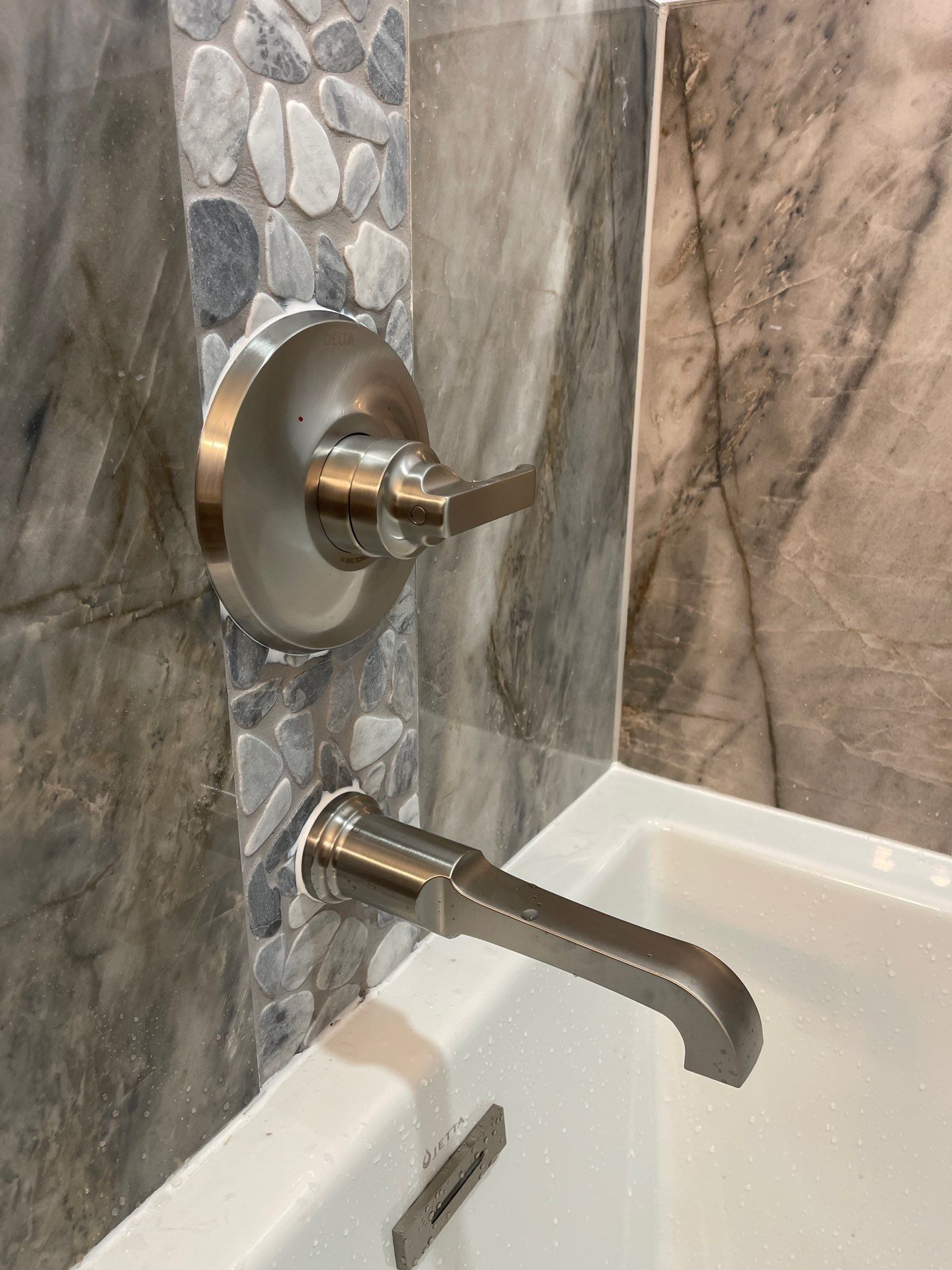 Modern chrome shower controls and tub spout on a marble-tiled bathroom wall