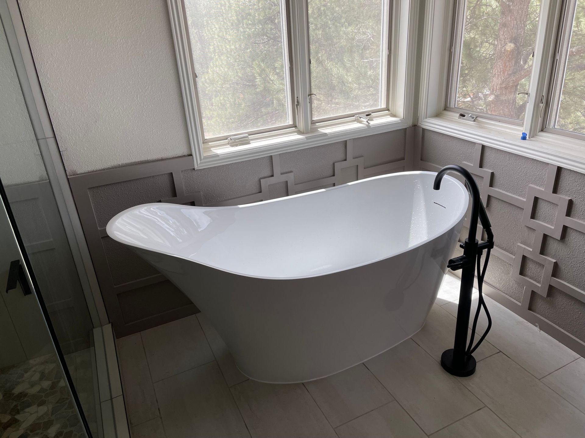 White freestanding bathtub by corner windows in a small bathroom