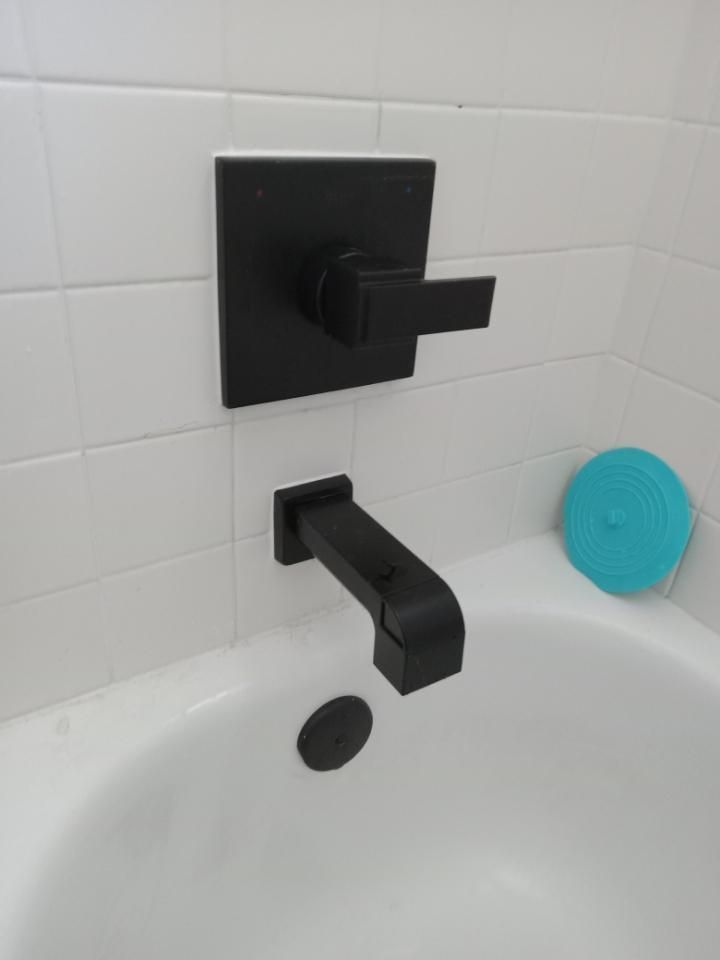 Modern black bathtub faucet and spout on white tile wall with blue scrubber in tub