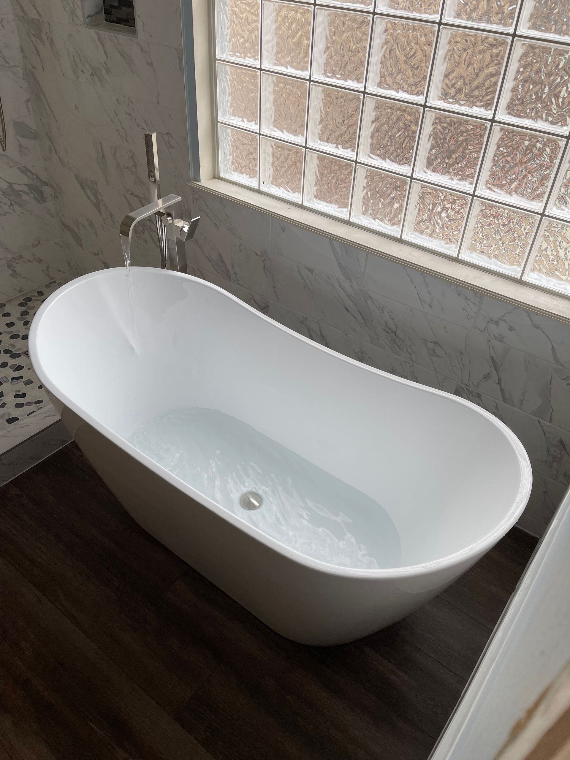 Modern white freestanding bathtub beside a frosted window in a bathroom with dark wood flooring