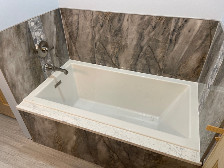 Modern white bathtub with marble-look tile walls and chrome faucet in a bathroom