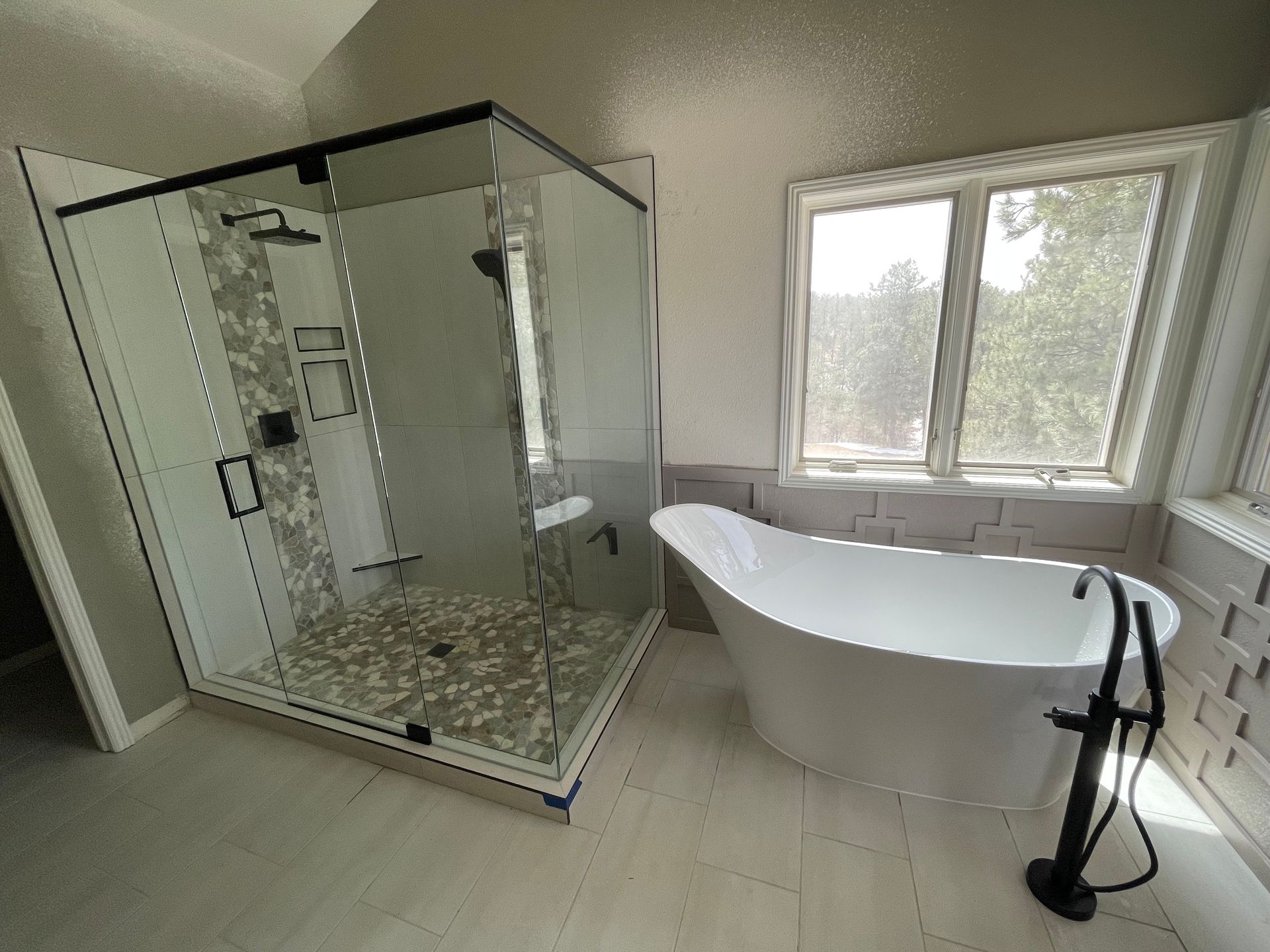Bathroom with glass shower, freestanding tub, and large window on a sloped ceiling.