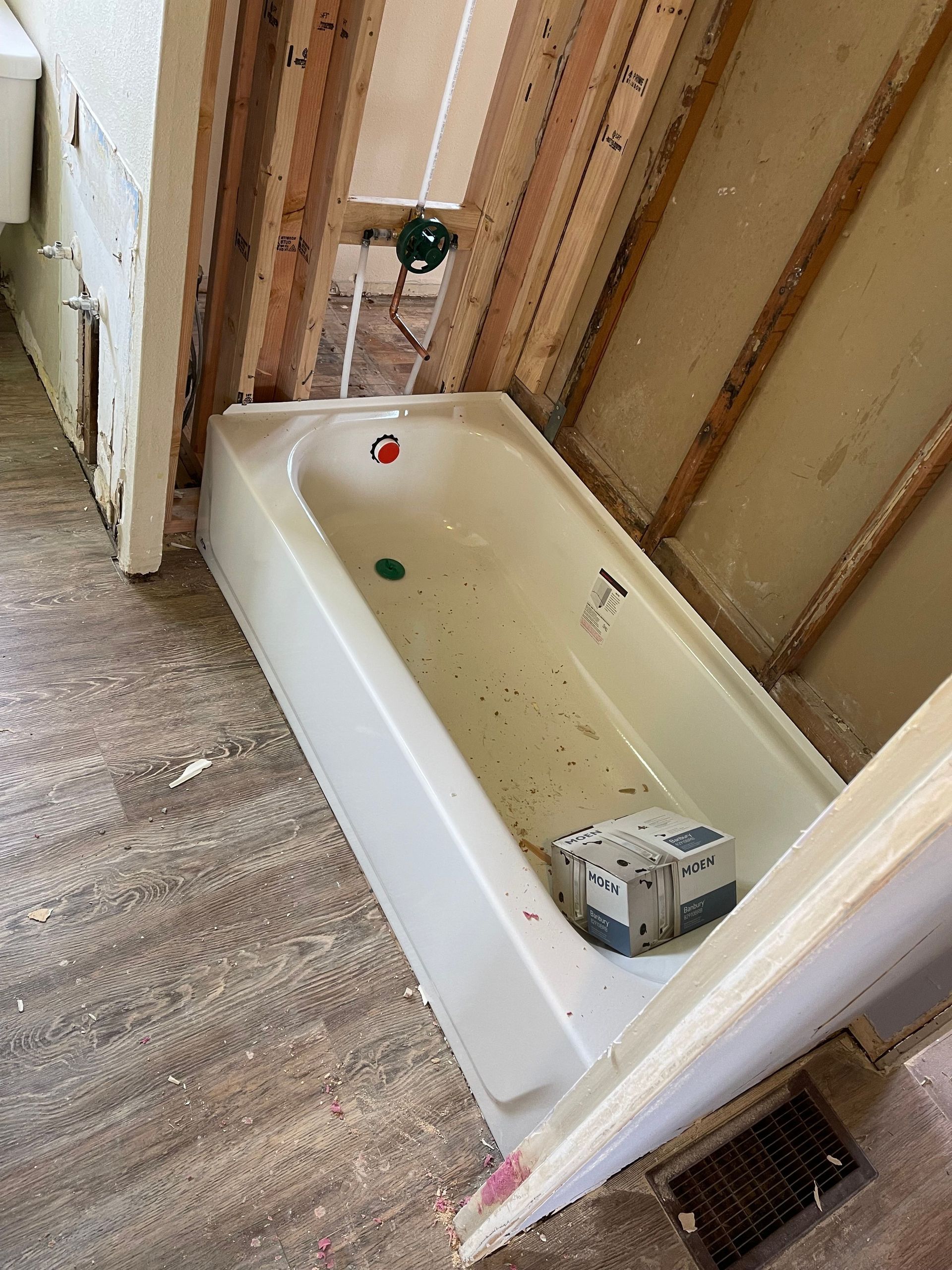 Old bathtub installed in an unfinished bathroom with exposed wall studs and debris on the floor