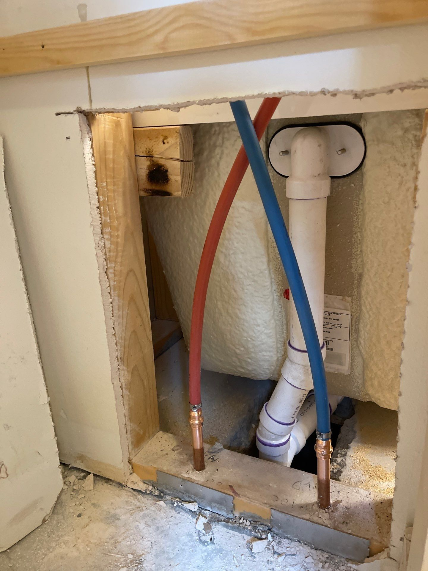 Open wall plumbing with red and blue pipes leading to a white drain assembly.