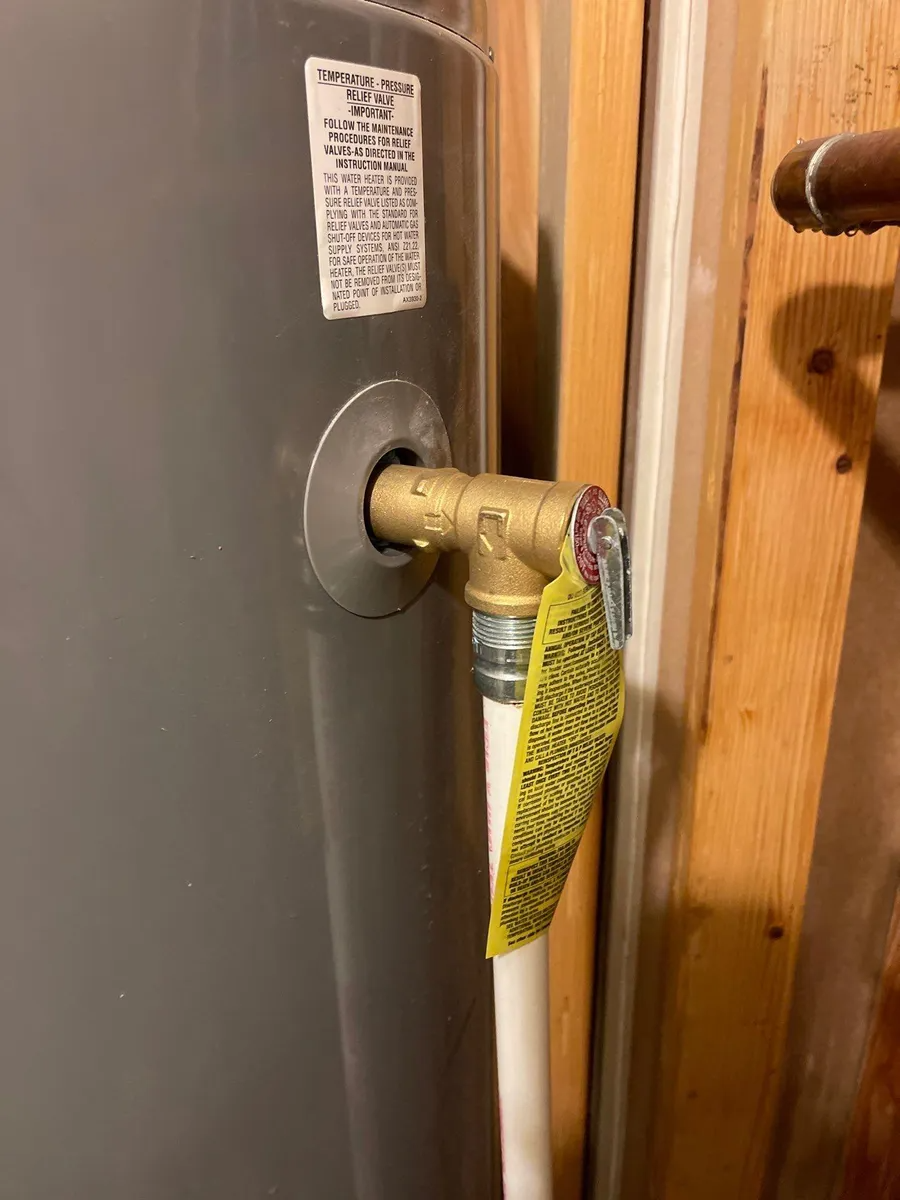 Water heater pipe connection with yellow tag and insulation in a wooden utility area