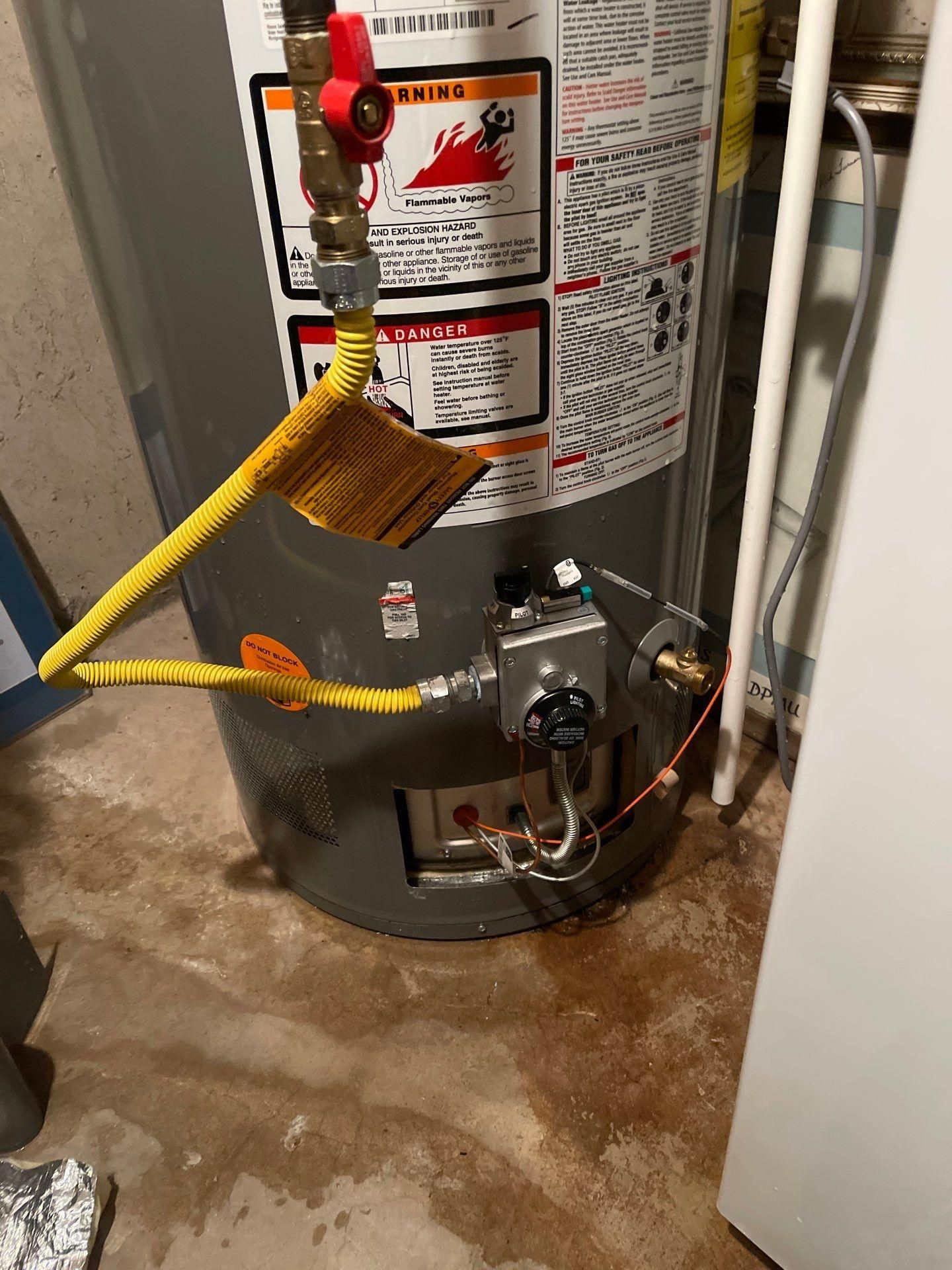 Water heater with yellow gas line and pilot assembly, showing a wet floor below.
