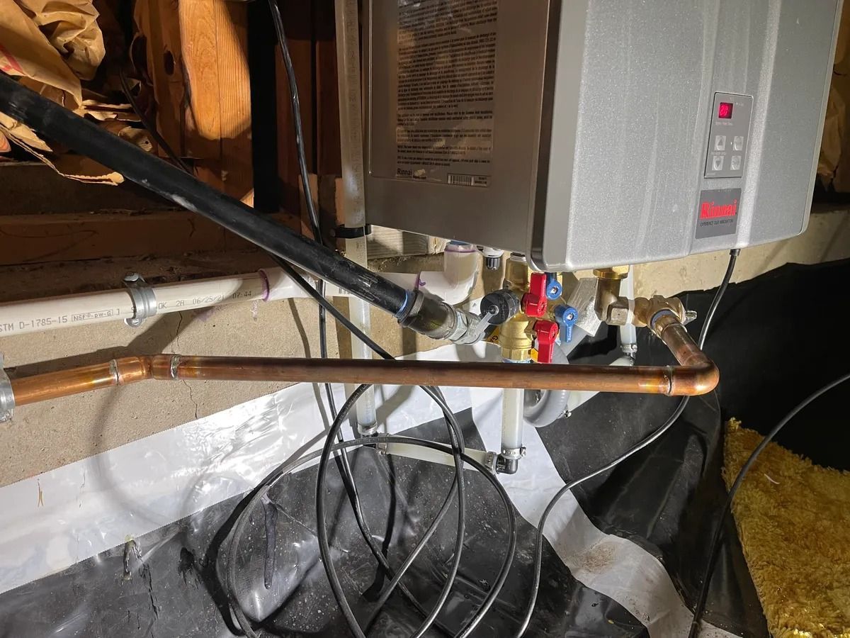 Cluttered basement with furnace pipes, wires, and a large box fan on the floor