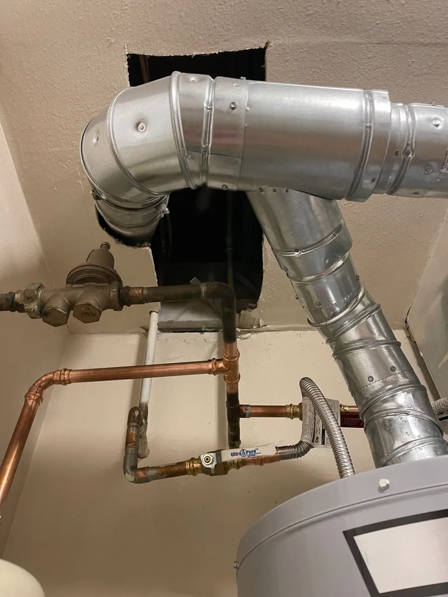 Exposed silver ductwork and copper pipes on a wall above a water heater in a utility room
