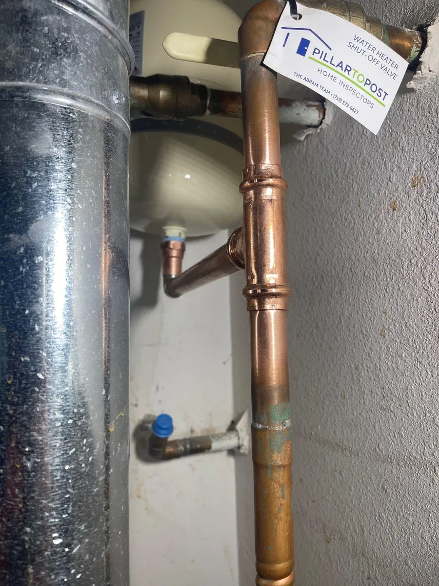 Copper and galvanized pipes with valves and a small hanging tag in a utility closet.