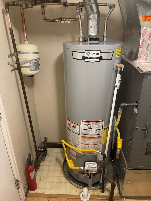Water heater in a utility closet with pipes, pressure tank, and a fire extinguisher on the floor.