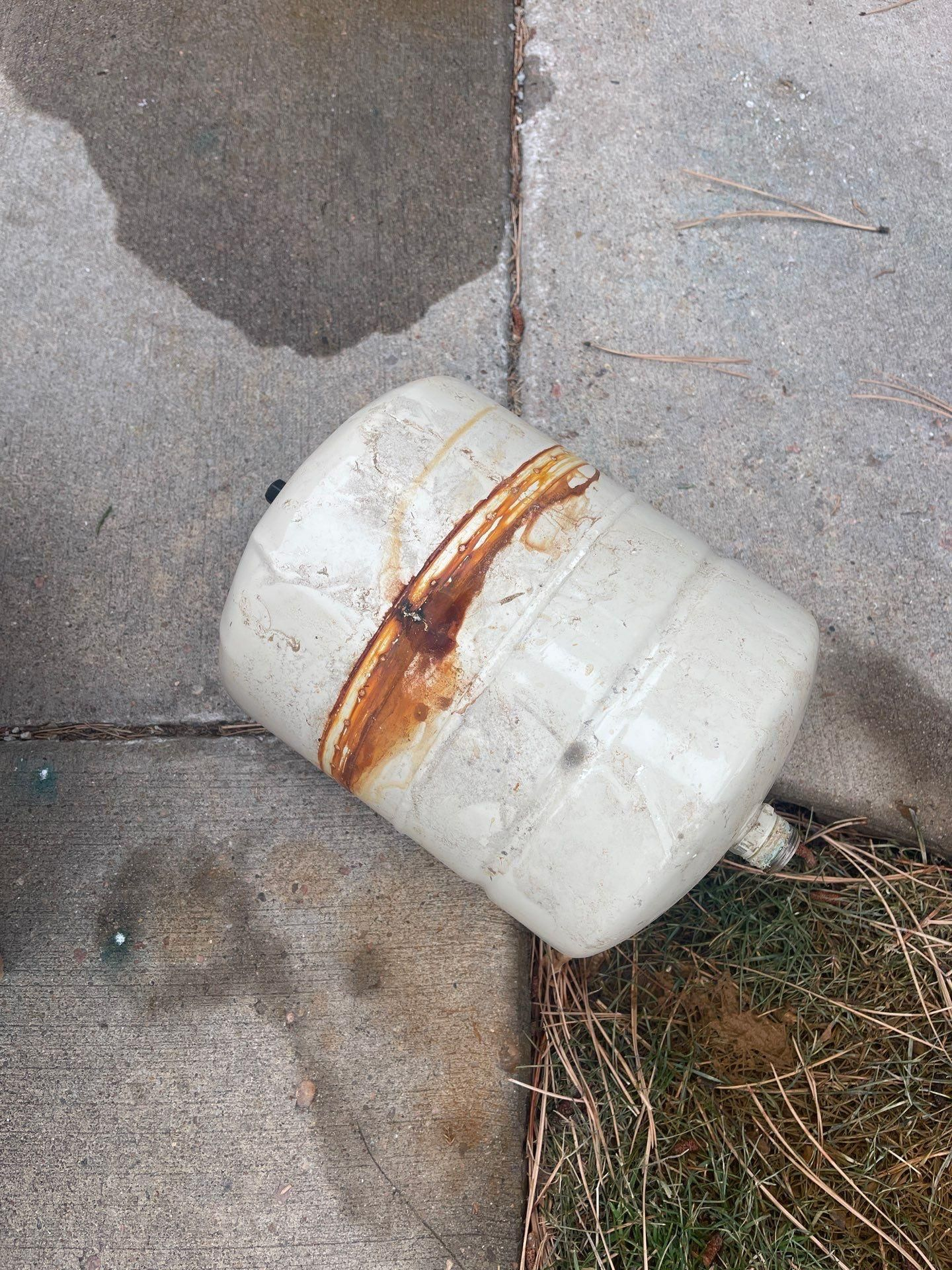 White plastic container with rusty brown stain lying on cracked pavement near dry grass