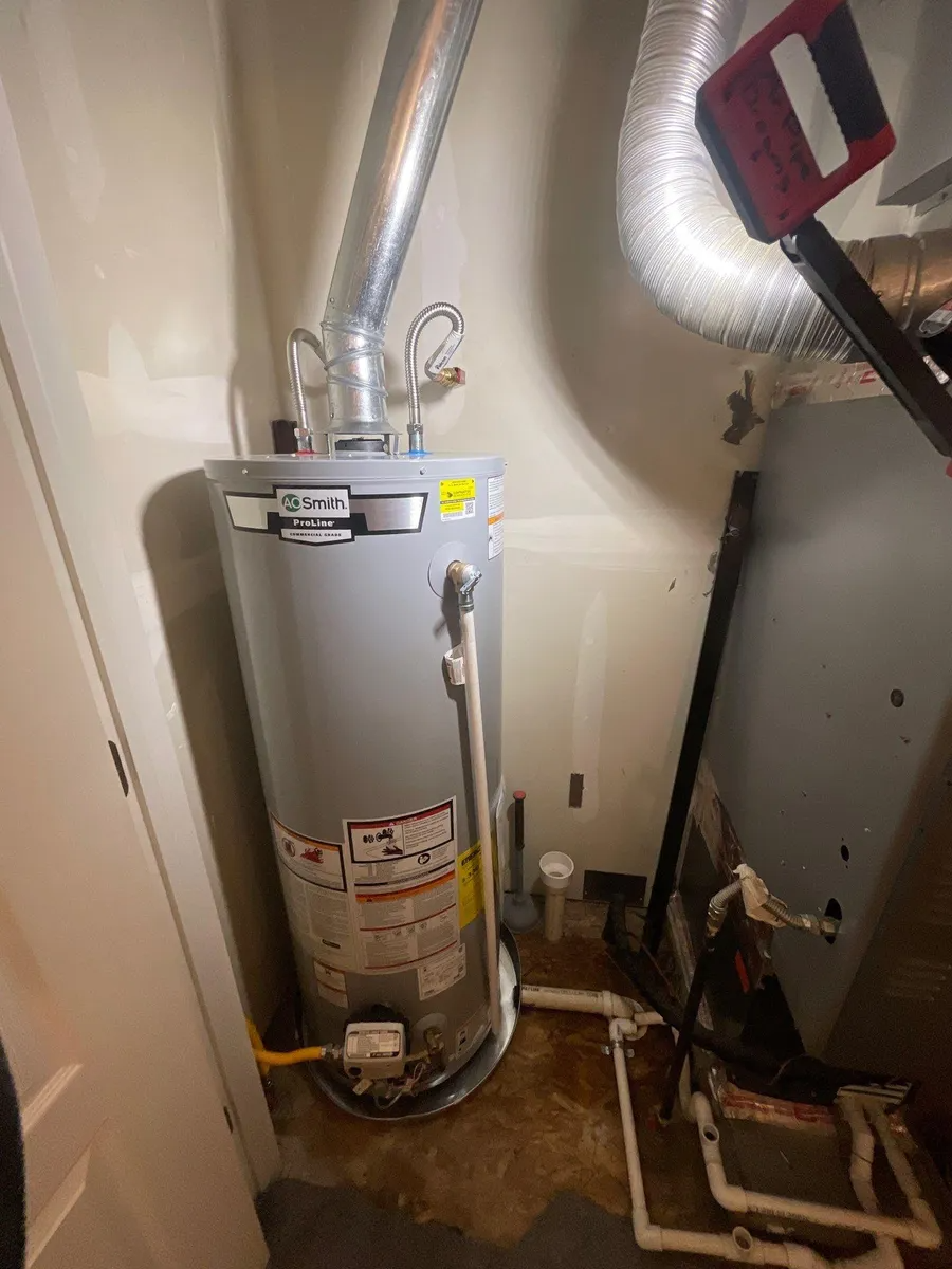 Water heater in a utility closet with metal vent pipes and exposed plumbing.