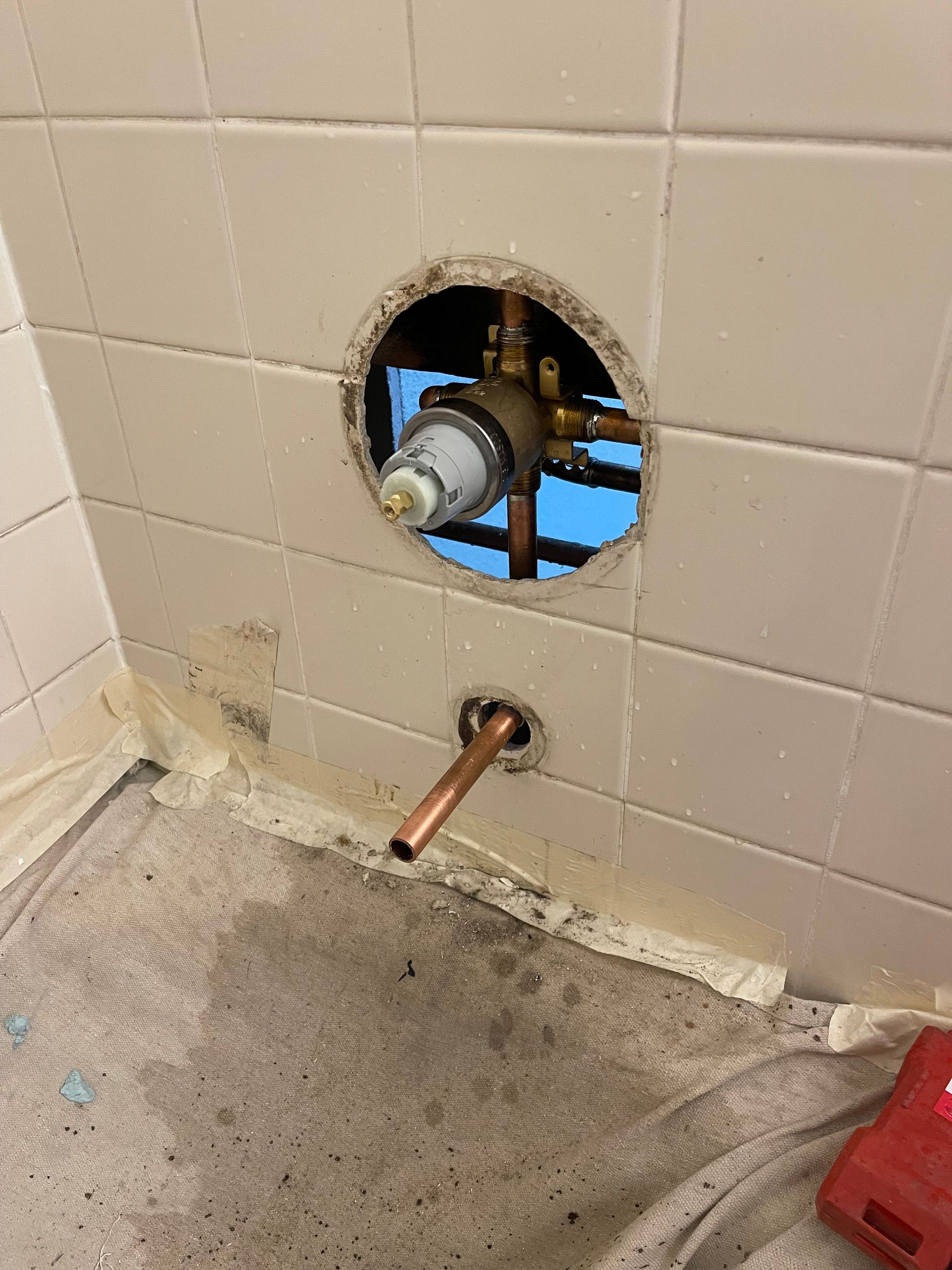 Bathroom wall with a round plumbing opening exposing pipes above a floor drain and concrete floor.