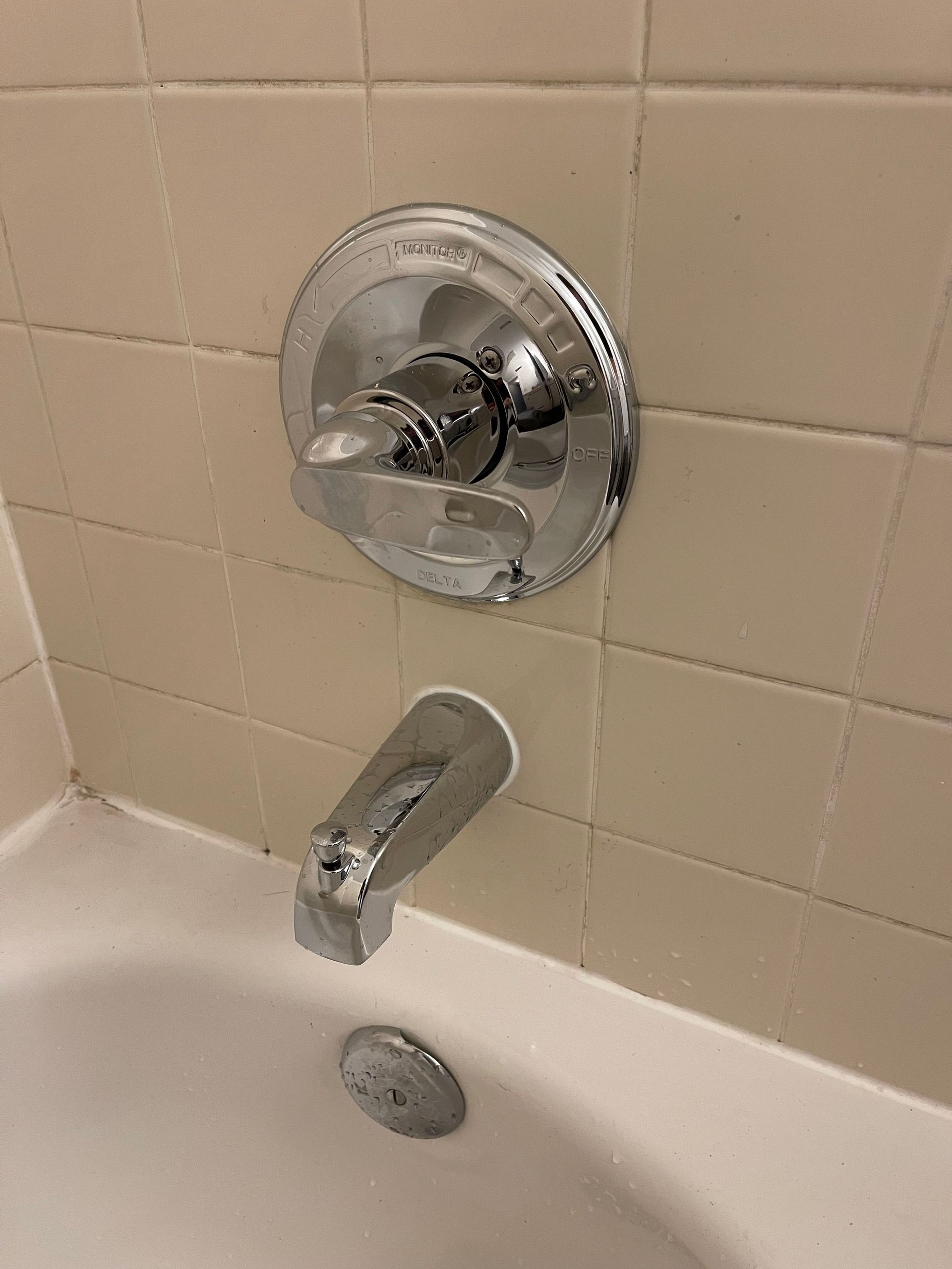 Bathtub shower faucet and spout on beige tile wall