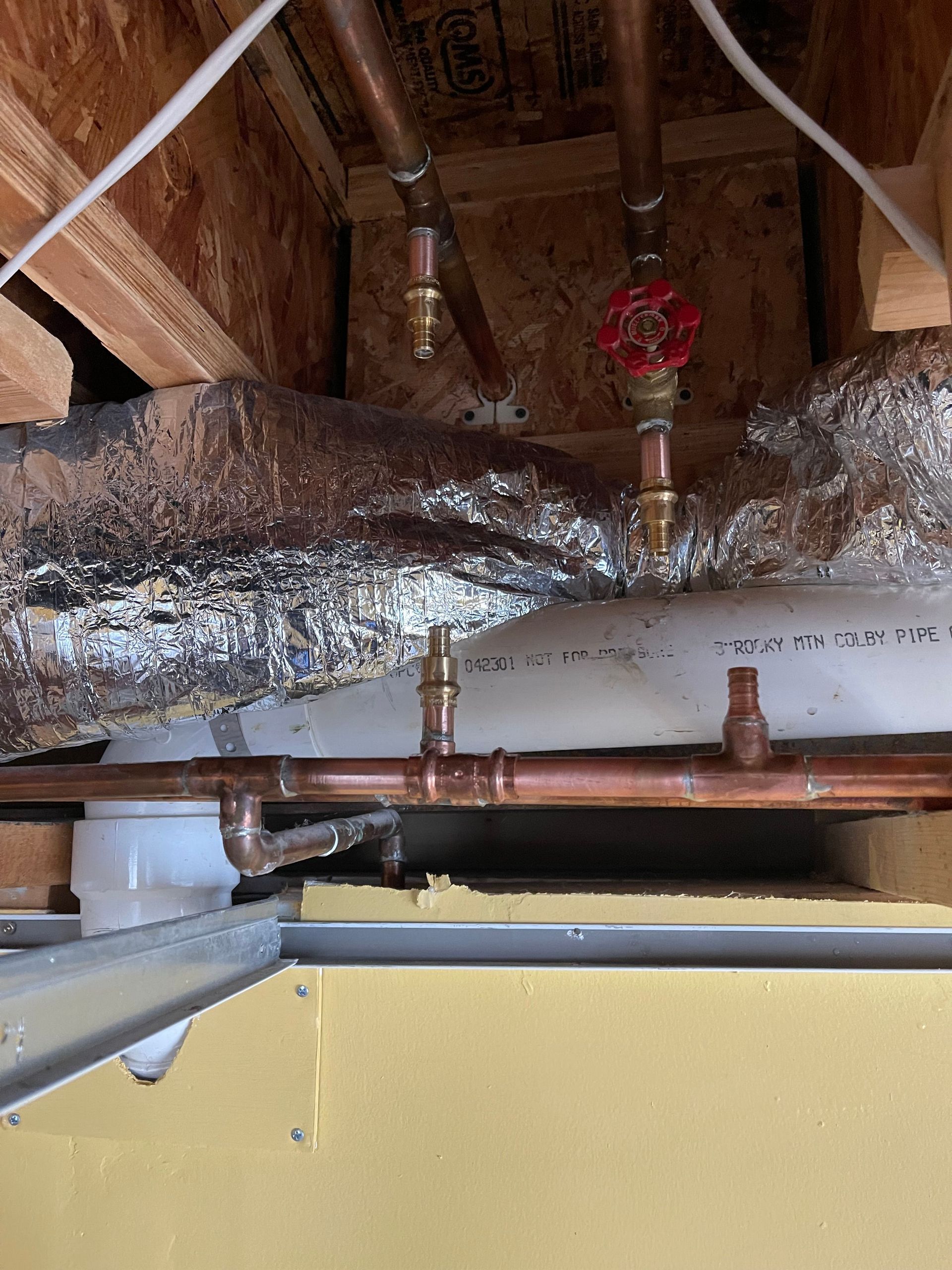 Attic with exposed copper piping, insulation, and a yellow wall panel beneath the roof framing
