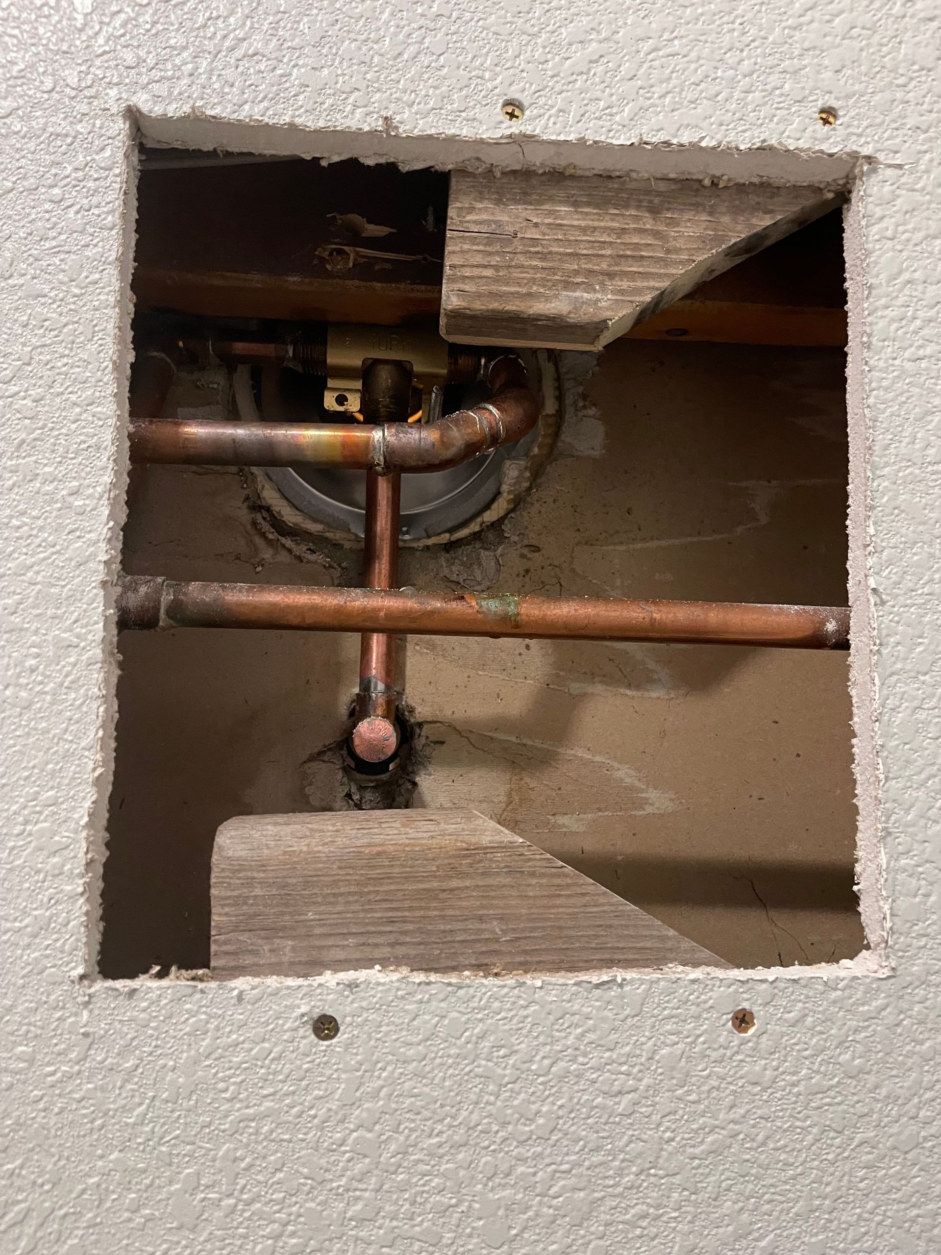 Open wall cutout showing copper plumbing pipes and fittings behind drywall.