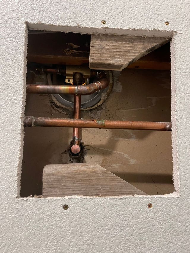Open wall cutout showing copper pipes and plumbing fittings inside a residential wall