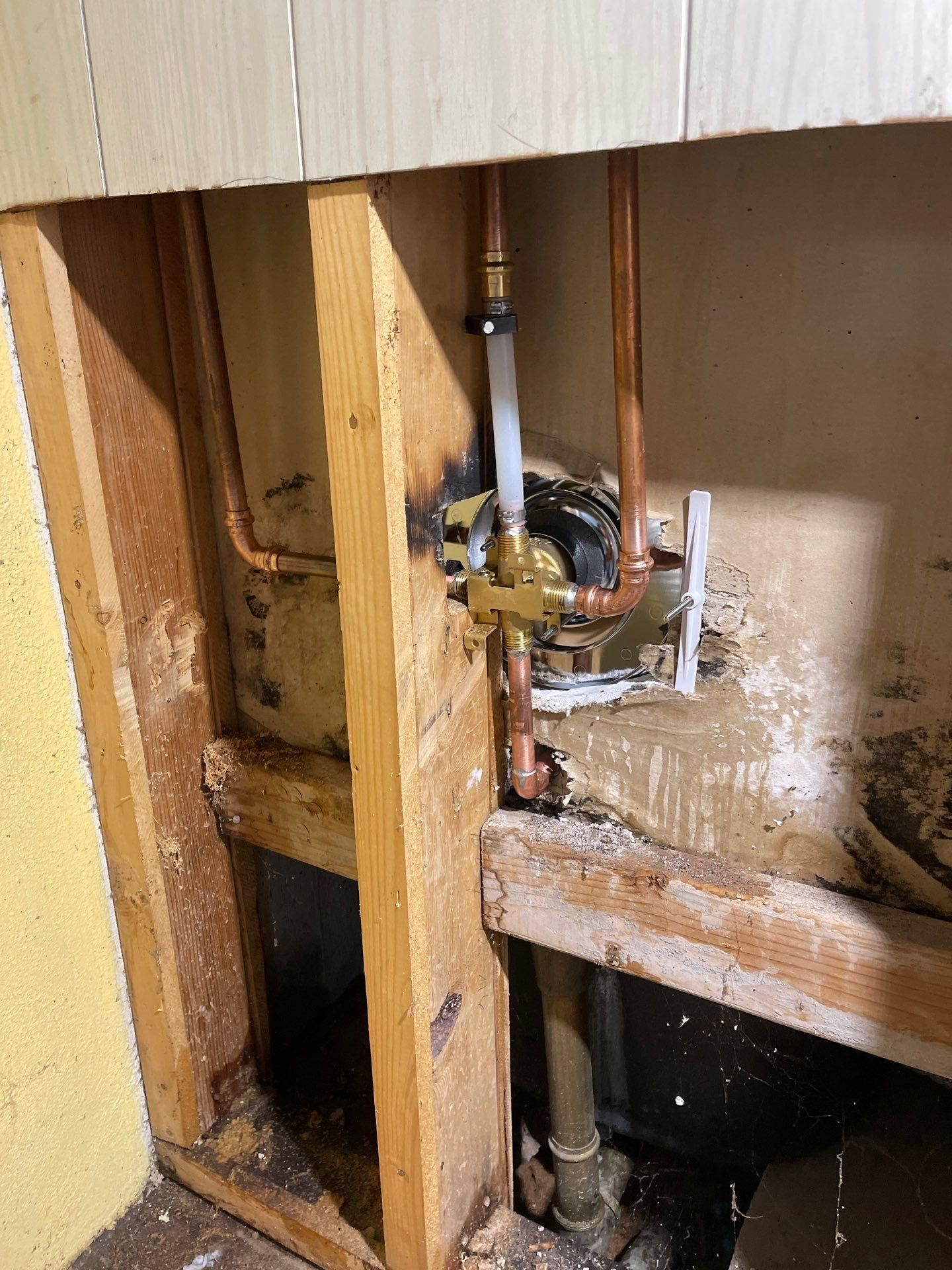 Exposed plumbing and wooden studs inside a wall cavity, with a white pipe and visible water damage.