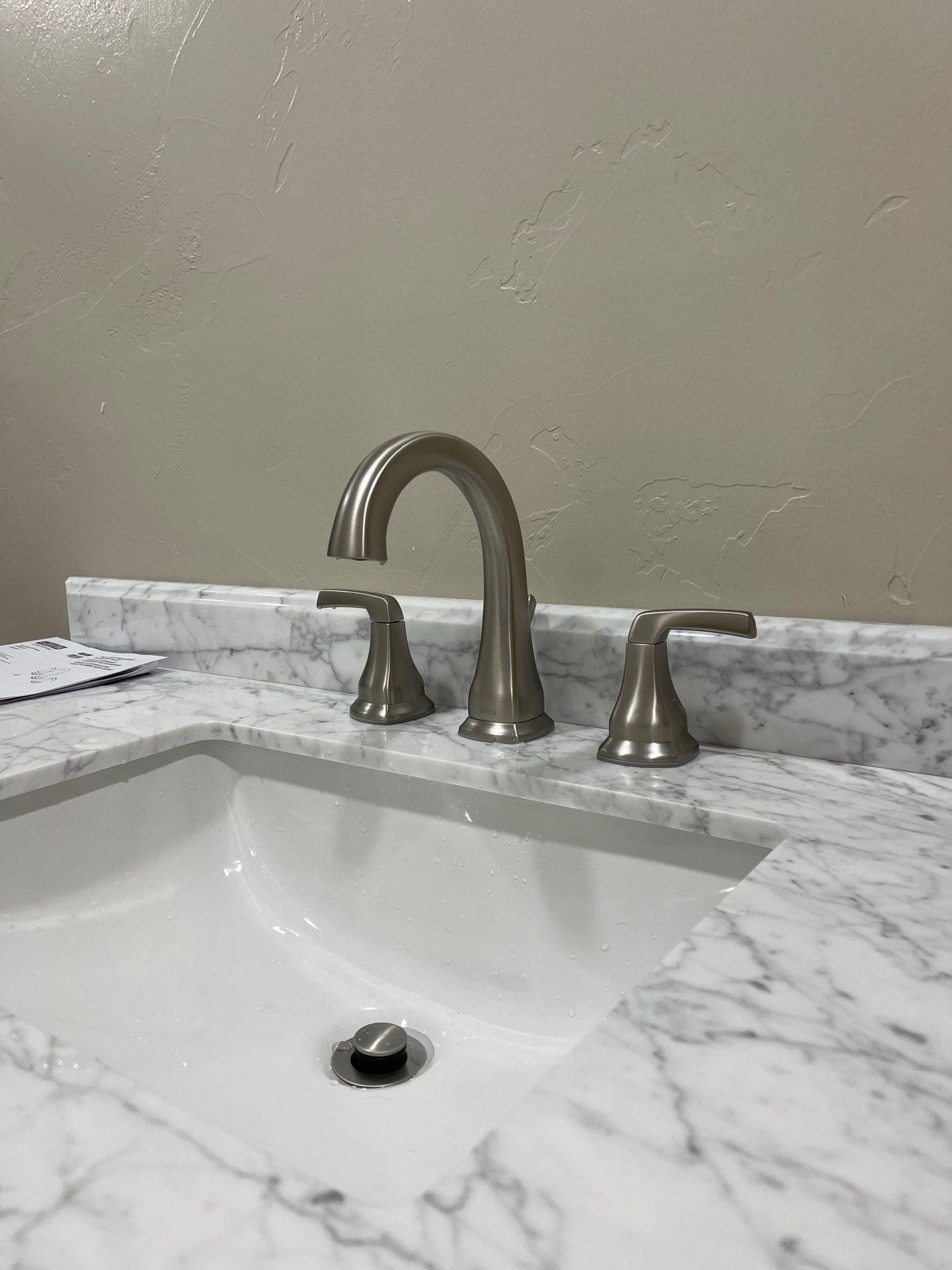Bathroom sink with white marble countertop and bronze faucet against a beige wall