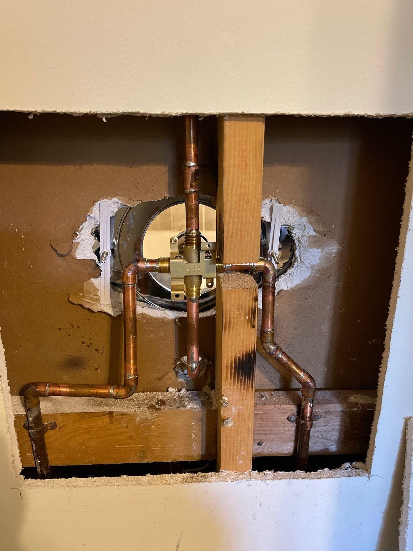 Exposed plumbing valves and pipes inside a wall opening, with rough drywall around them.