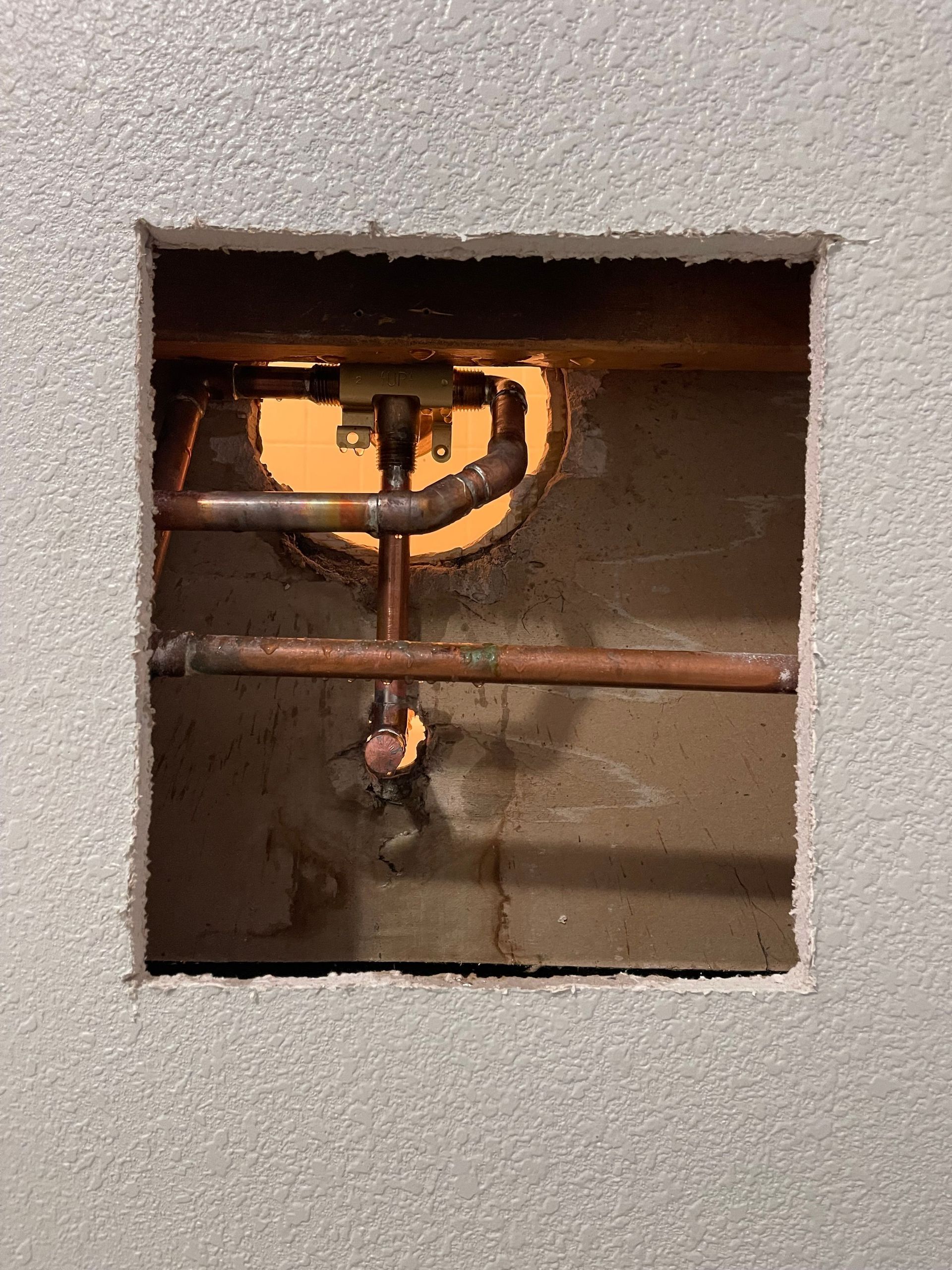 Square wall cutout exposing copper pipes and valves inside a utility cavity.